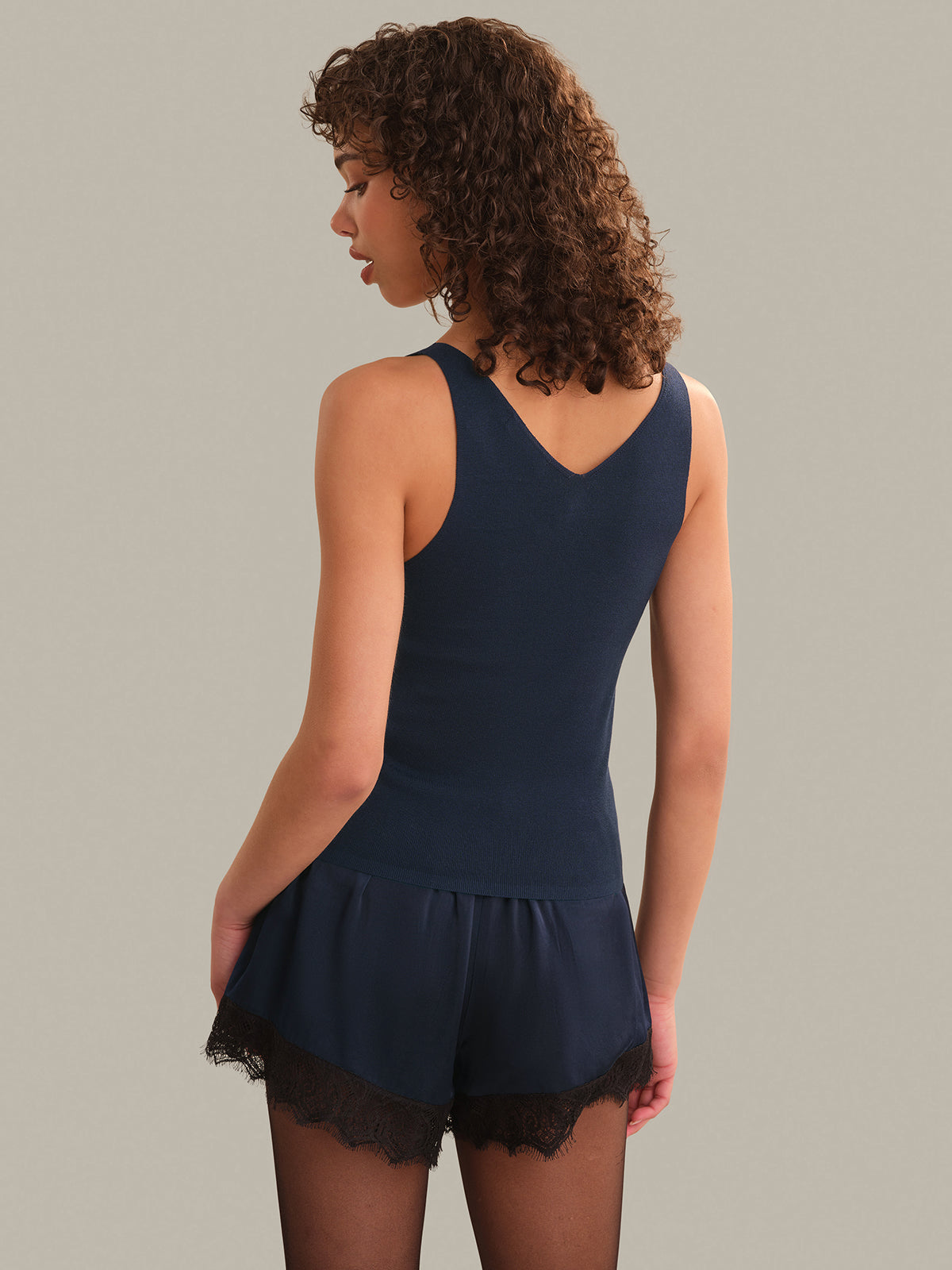 Woman wearing a navy blue tank with lace trim on a plain background