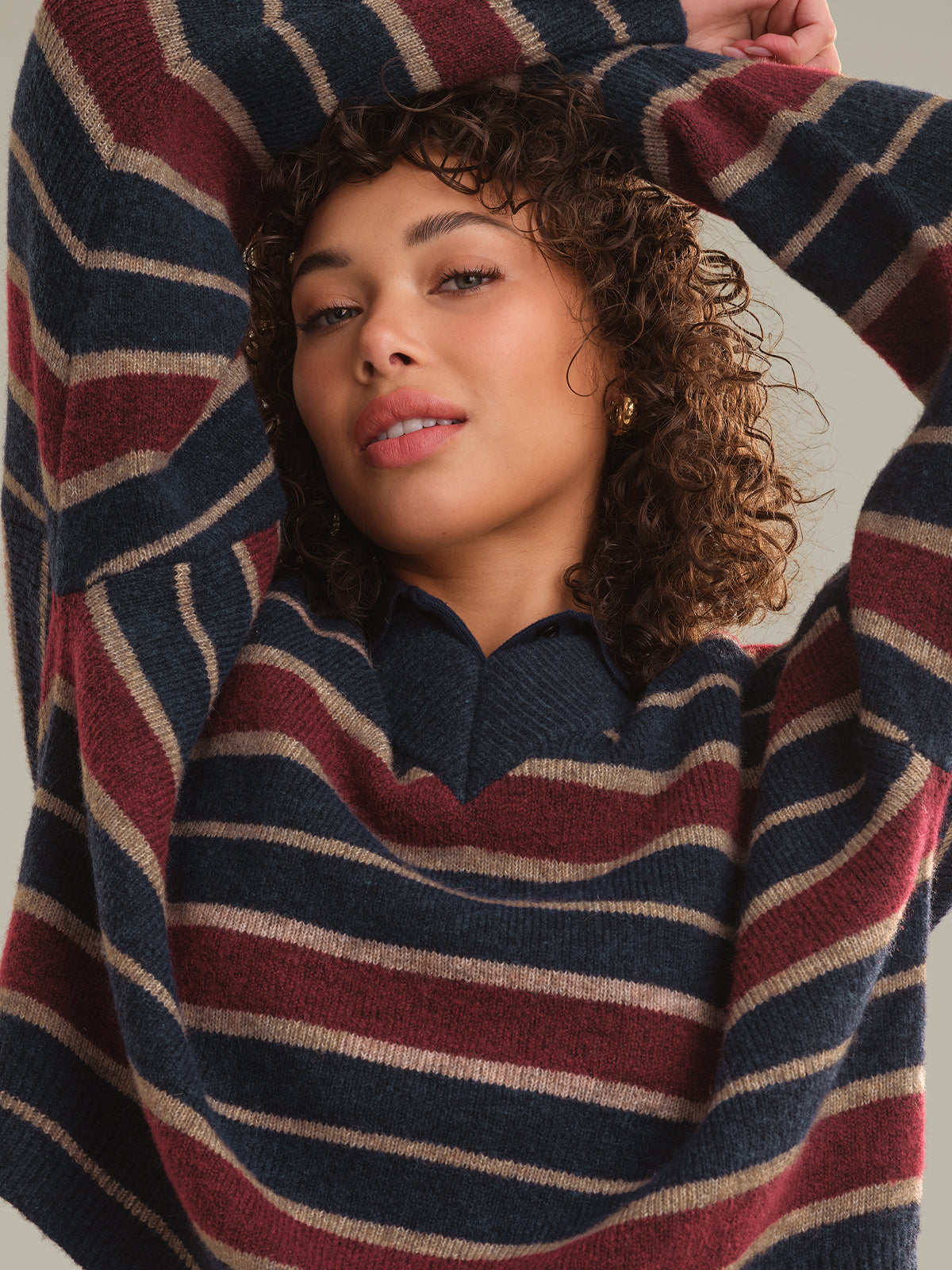 A close-up of a woman wearing a cozy knit sweater with horizontal stripes in navy blue, burgundy red, and cream.