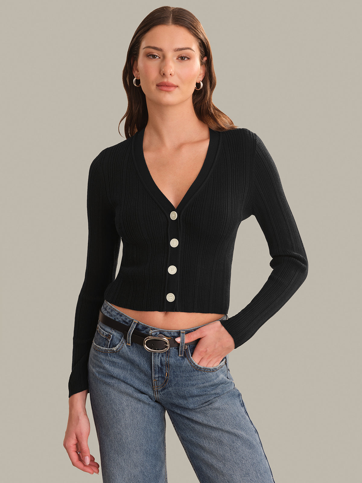 Woman wearing a black cardigan with white buttons and blue jeans on a gray background