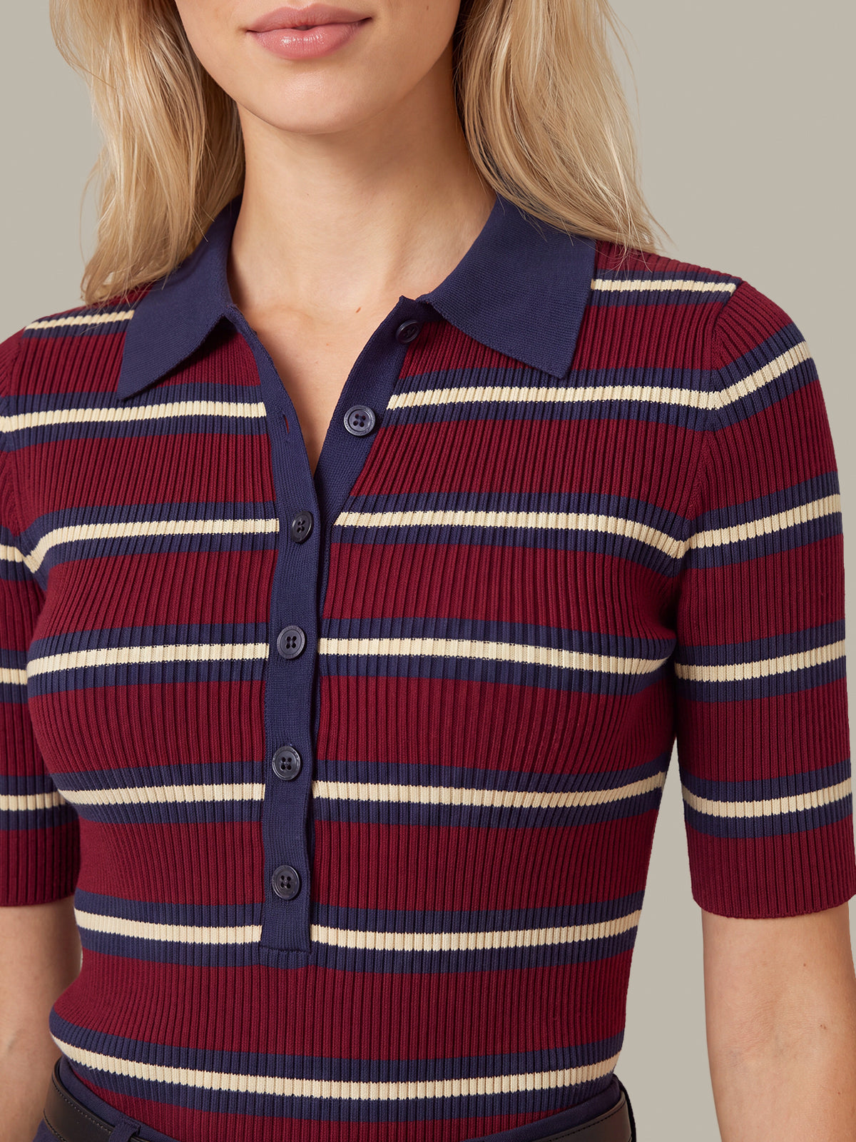 A close-up of a woman wearing a ribbed short-sleeve polo shirt with horizontal navy, burgundy, and cream stripes, featuring a solid navy collar and button placket.