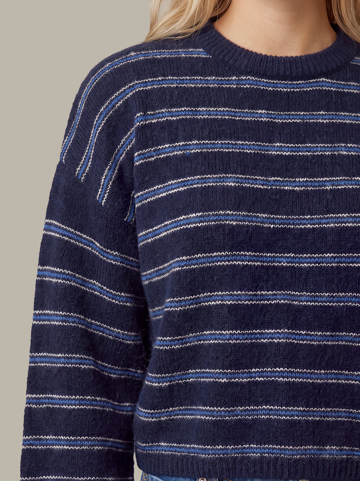A close-up of a person wearing a navy blue knit sweater with thin horizontal white and light blue stripes.