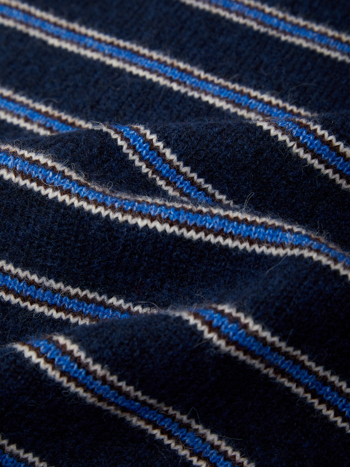 Close-up of a navy blue knit fabric with diagonal stripes in light blue, white, and thin brown lines.