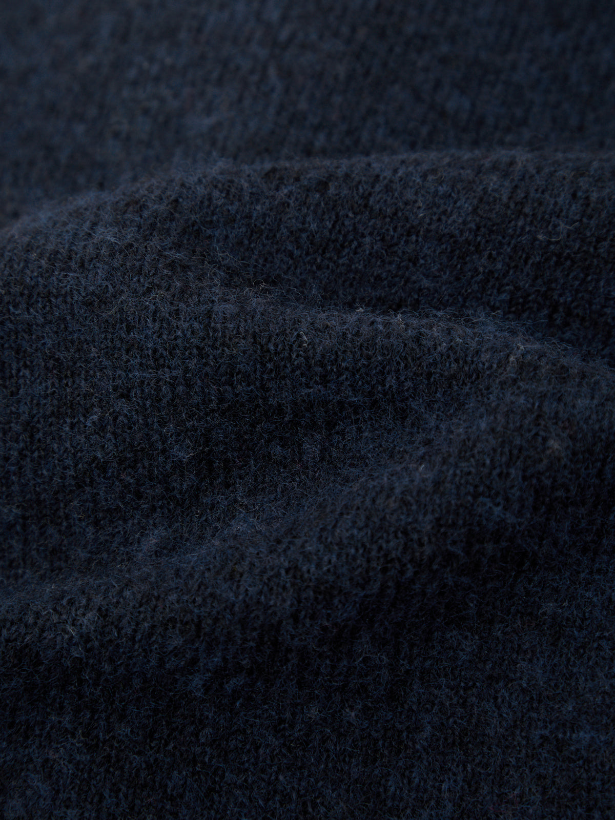 A close-up of dark navy blue knit fabric with soft folds and a textured, fuzzy surface.