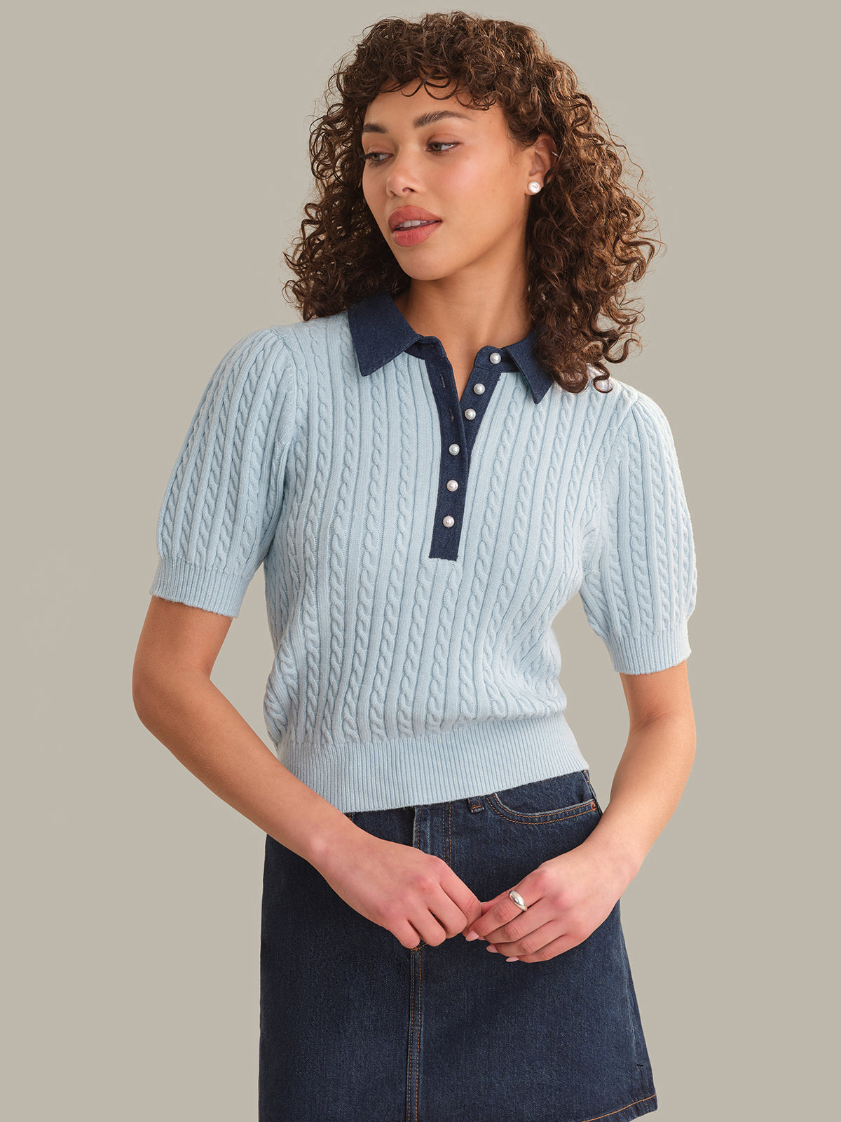 Woman wearing a light blue knitted polo shirt with a dark collar against a neutral background