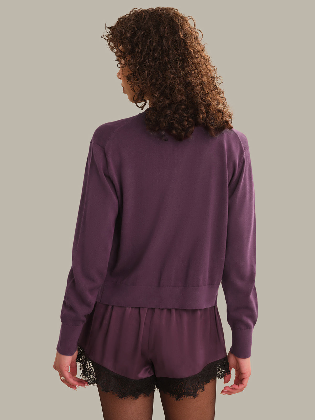 Person wearing a purple cardigan with black lace trim on a plain background