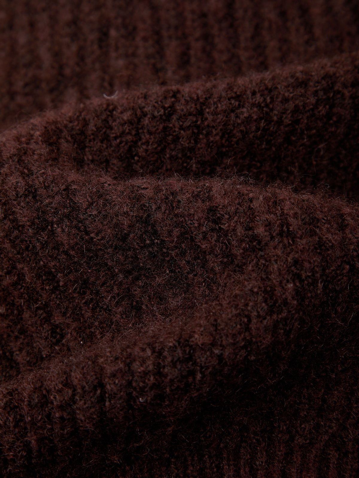 Close-up of a dark brown ribbed knit fabric texture with soft folds and a fuzzy, plush surface.