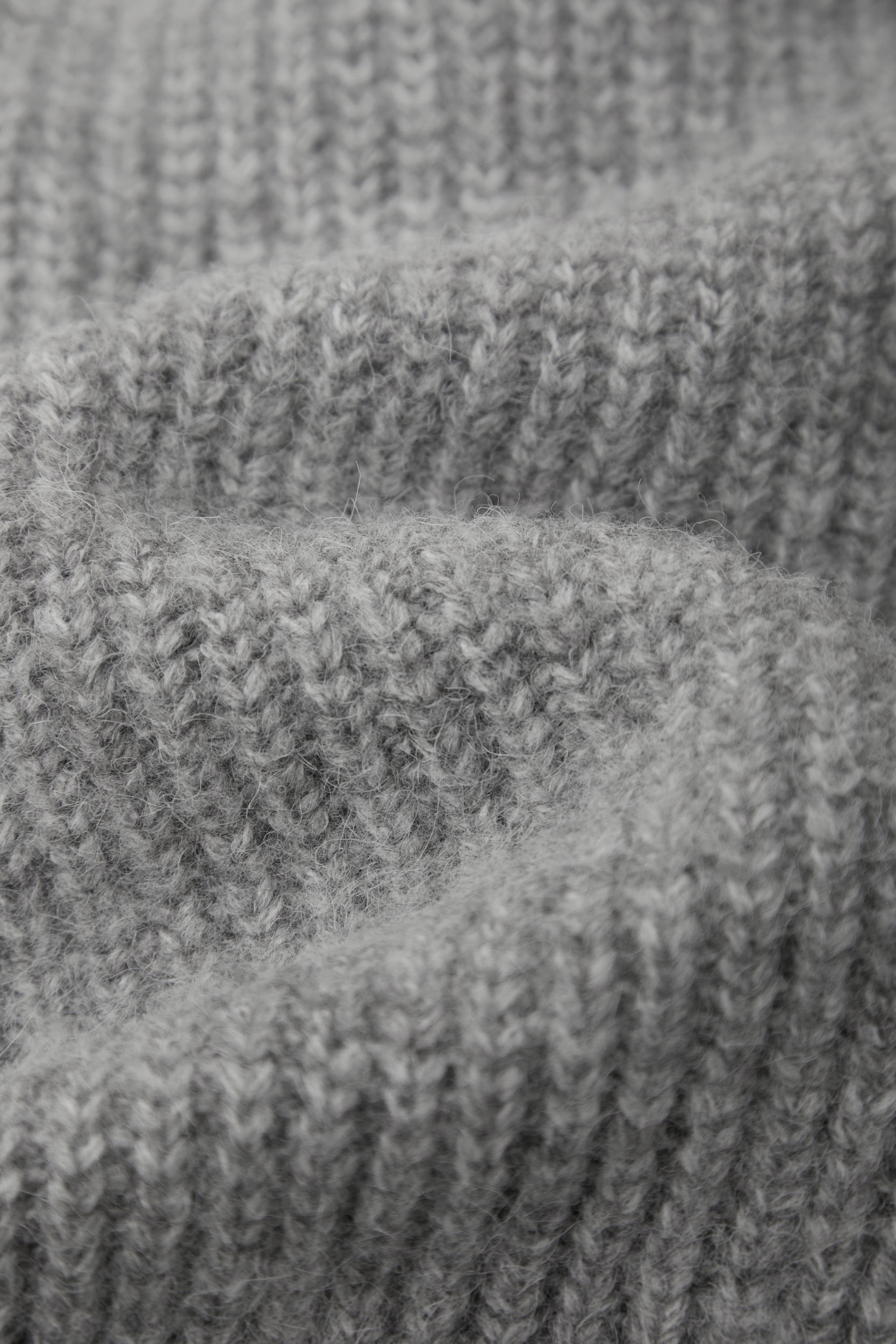 Close-up of a gray ribbed knit fabric texture with soft folds and visible yarn detail.