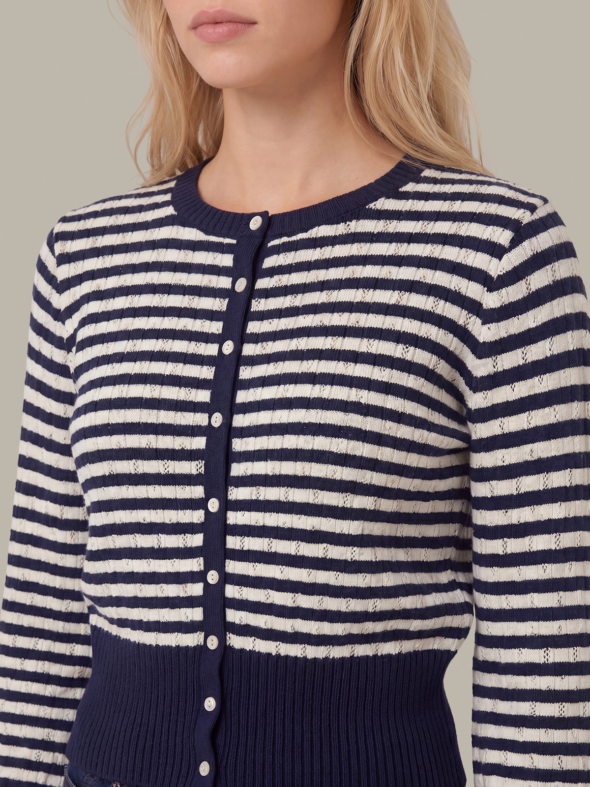 A close-up of a woman wearing a navy and cream striped knit cardigan with a button-front closure and ribbed hem.