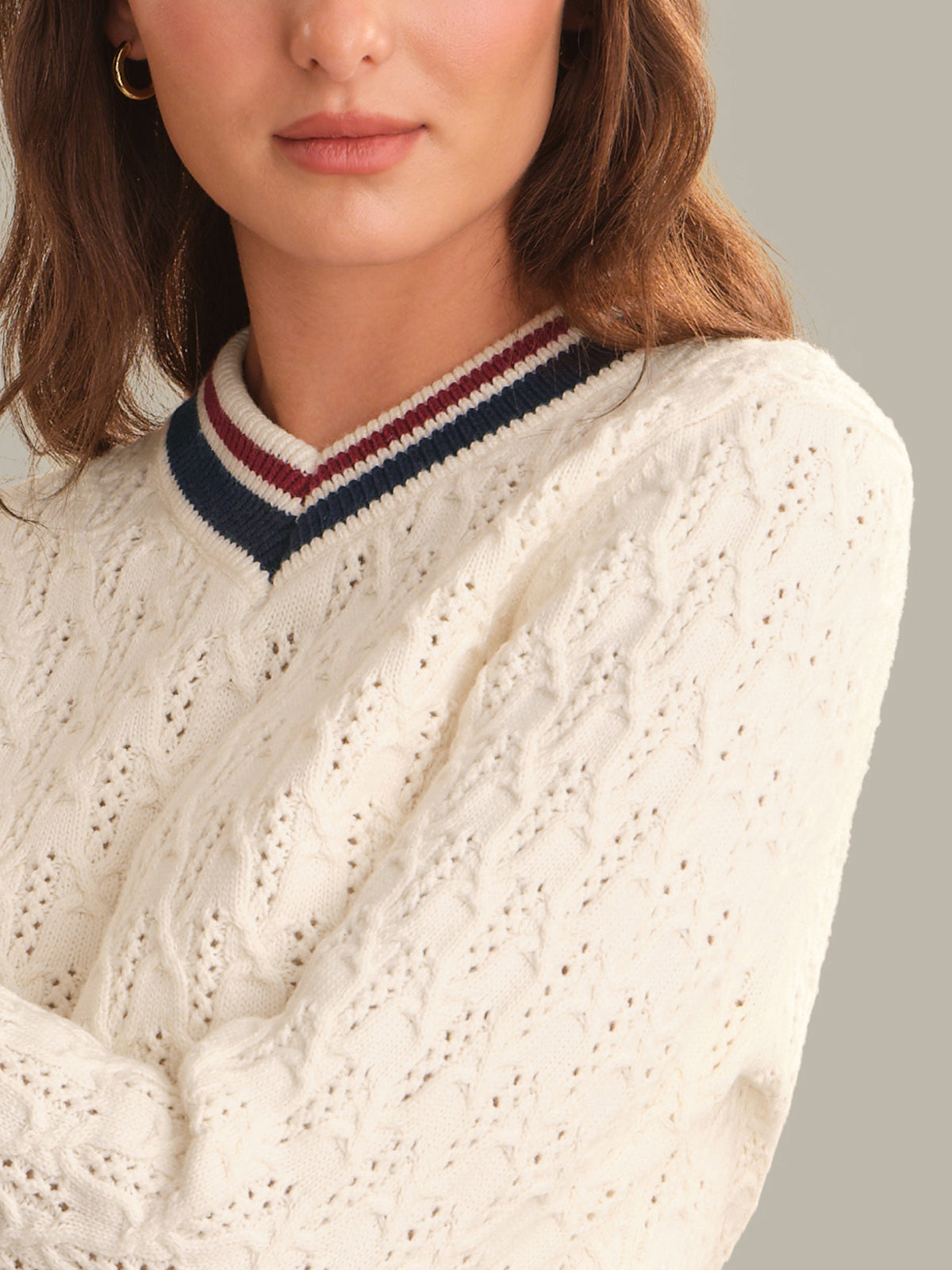 Close-up of a woman wearing a cream cable-knit sweater with a navy, burgundy, and cream striped v-neck collar.