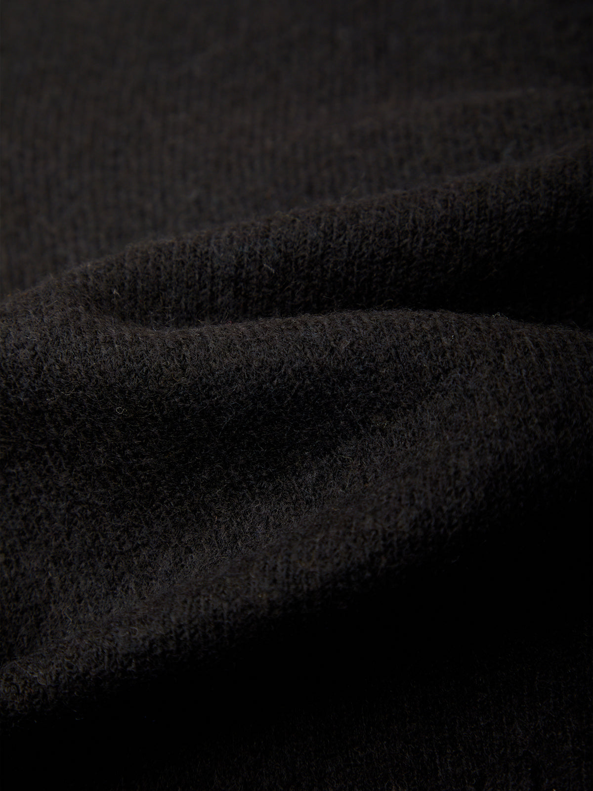 A close-up of dark charcoal gray knit fabric with soft folds and a fine ribbed texture.