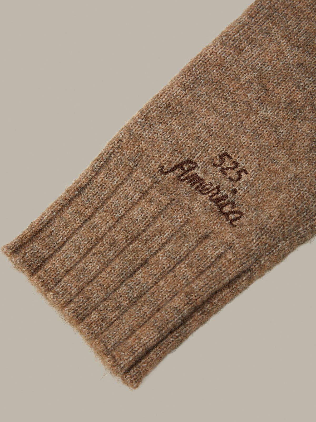 A close-up of a ribbed knit sock cuff in a warm camel brown color, featuring the embroidered text '525 America' in dark brown.