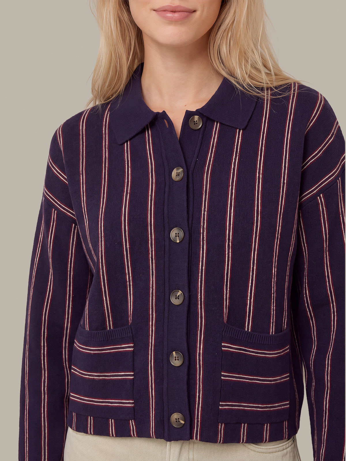 A woman wearing a cropped knit cardigan with vertical pink stripes on a dark navy blue base, featuring a button-front closure and front pockets.