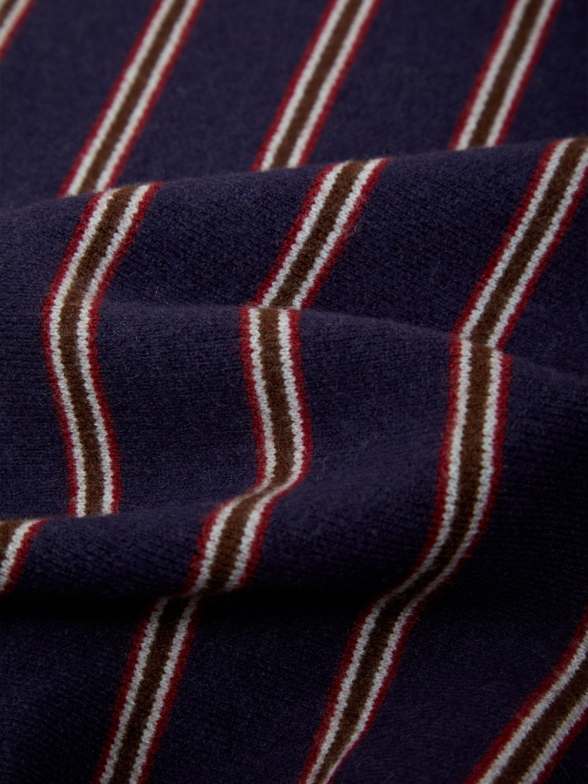 A close-up of a navy blue knit fabric with vertical stripes in brown, white, and red.