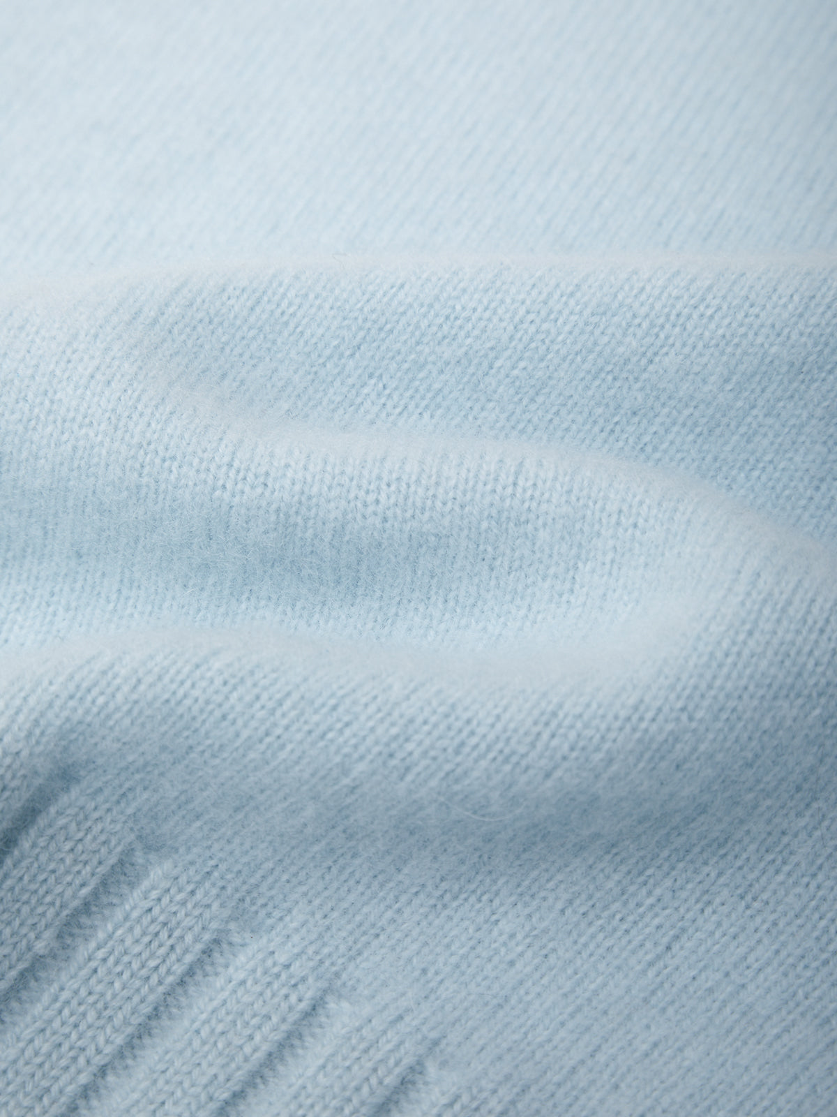A close-up of light blue knit fabric with soft folds and ribbed texture.