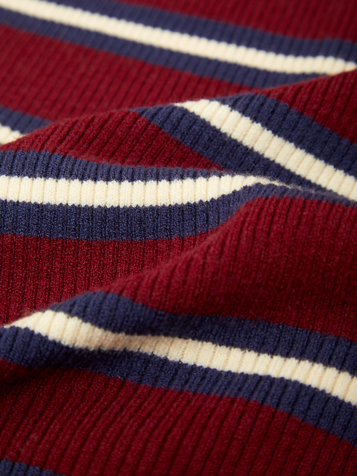 Close-up of a ribbed knit fabric with horizontal stripes in deep red, navy blue, and cream.