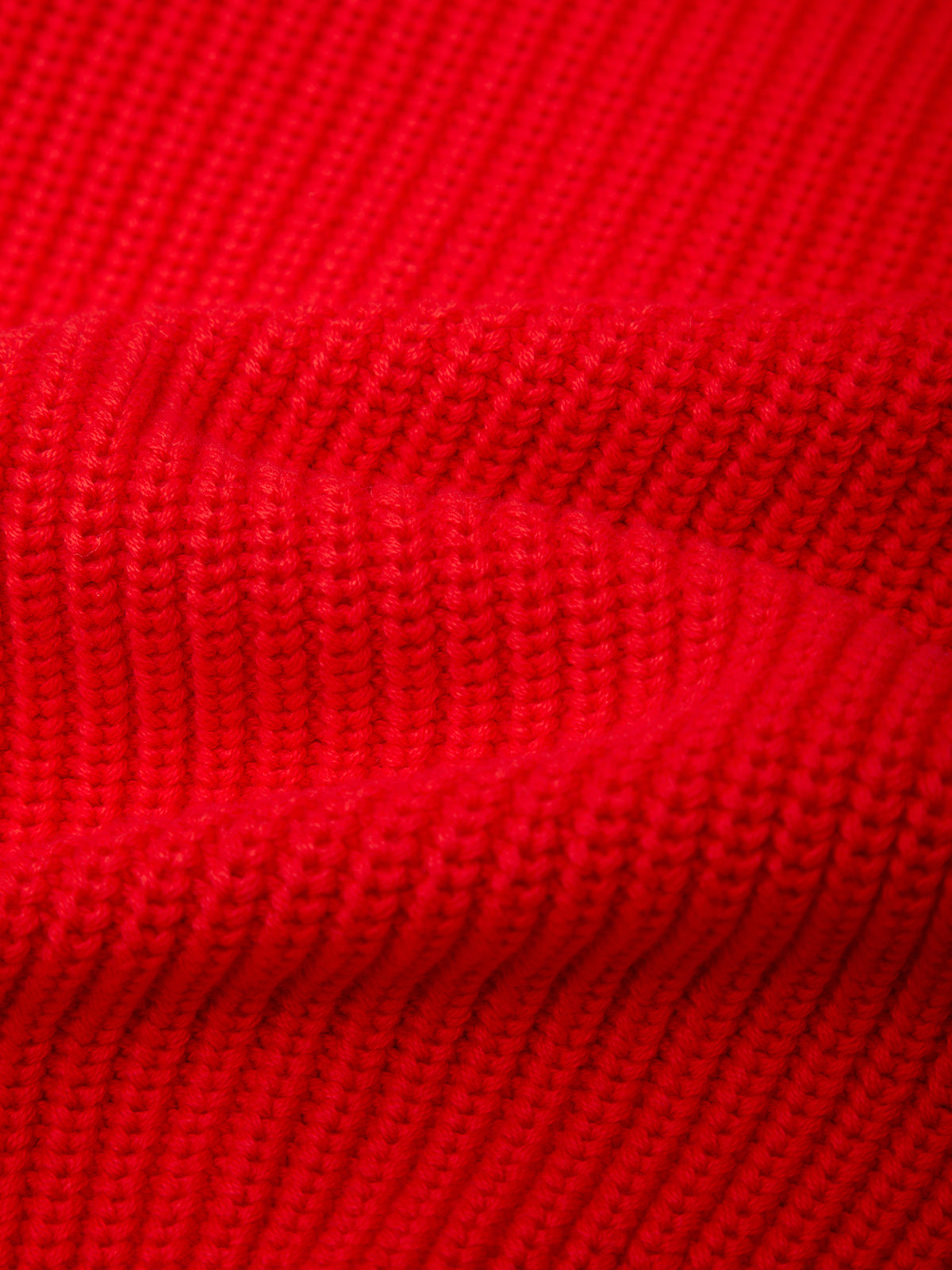 A close-up of bright red ribbed knit fabric with a textured waffle pattern and soft folds.