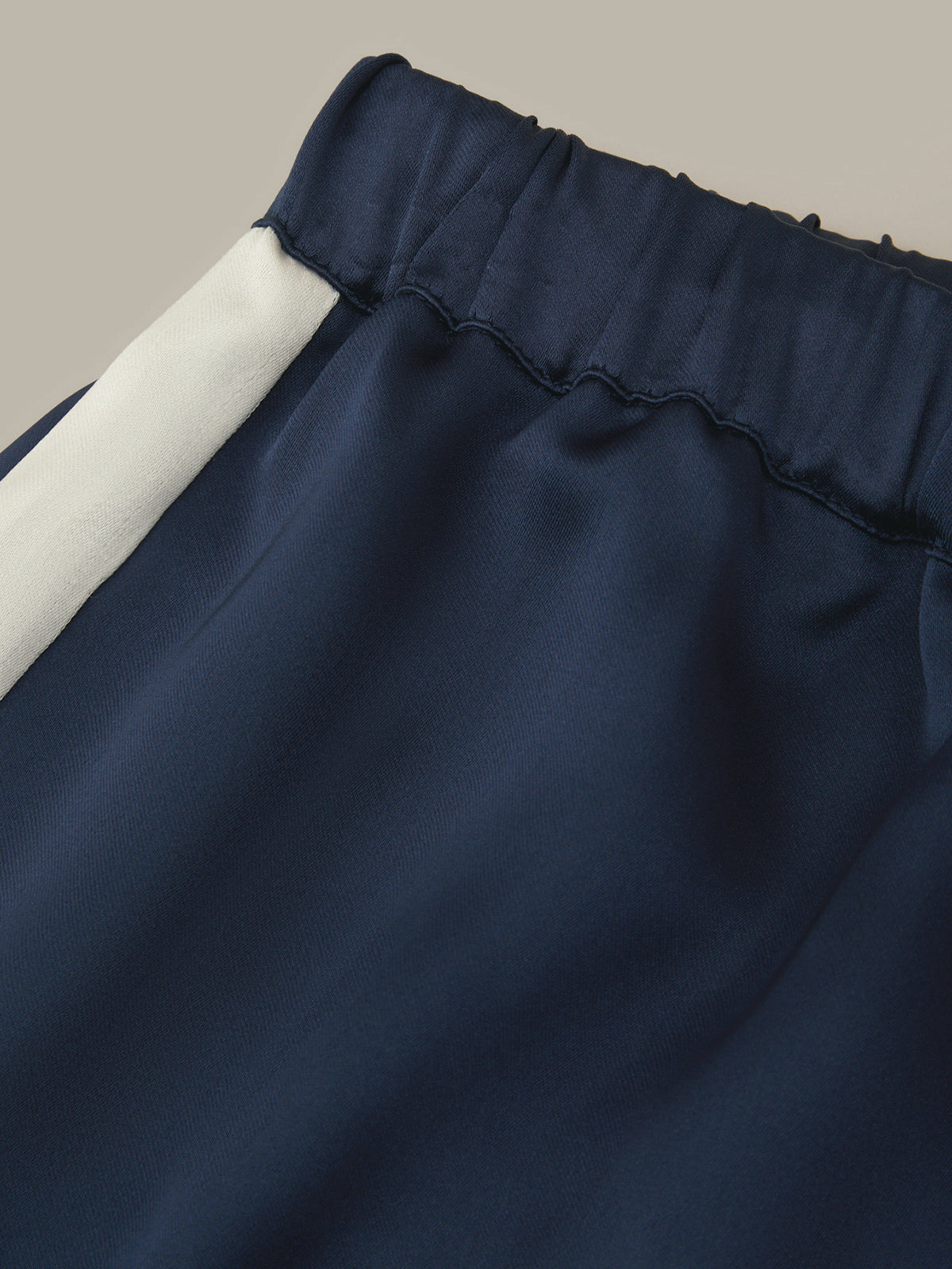 Close-up of navy blue fabric with a white side panel and an elastic gathered waistband, shown against a plain beige background.