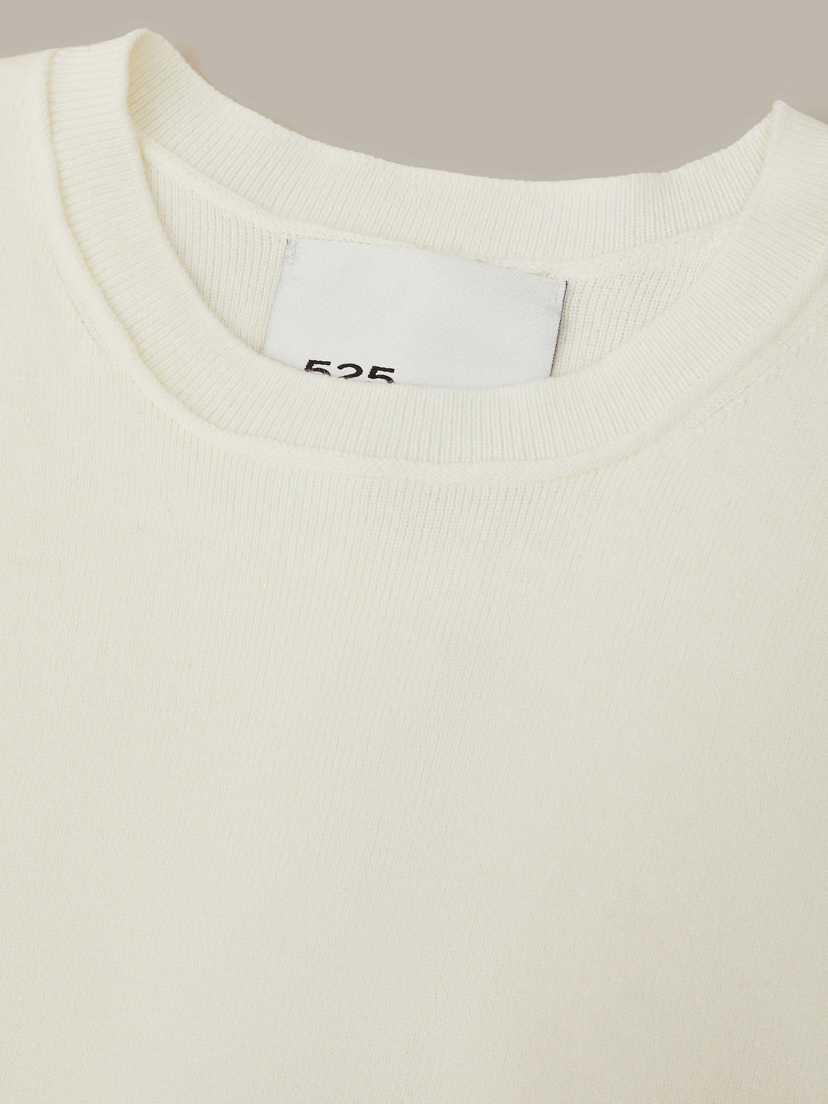 Close-up of a white sweater with a brand label on a neutral background