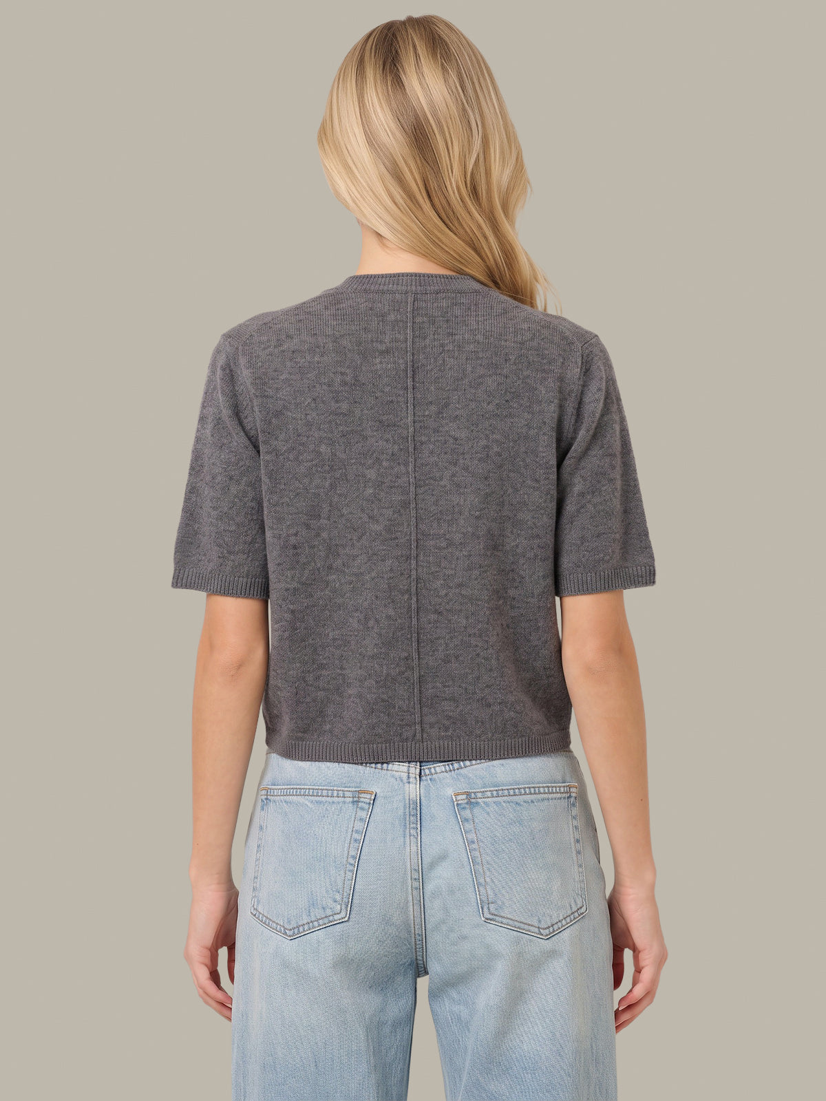 A woman viewed from the back wearing a dark gray short-sleeve knit top and light blue jeans against a solid beige background.