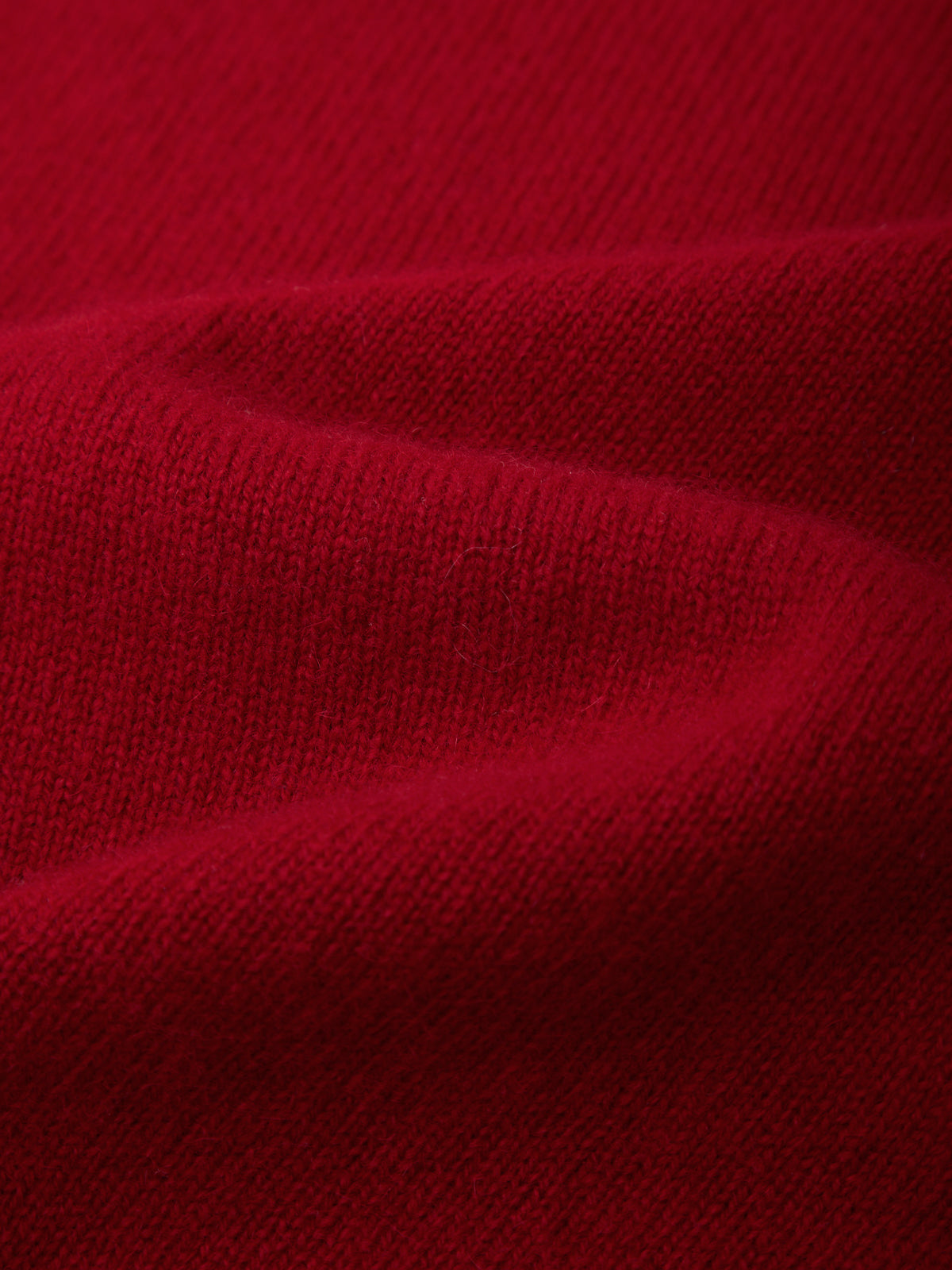 A close-up of deep red knit fabric with soft folds showing the texture and color.