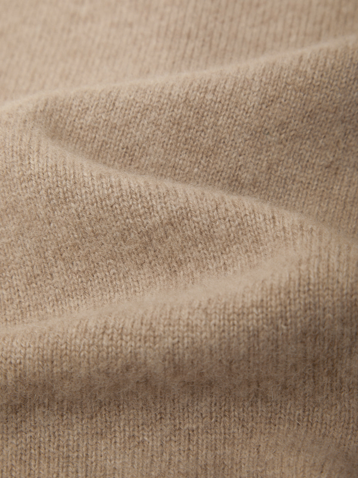 Close-up of a soft knit fabric in a warm light beige or oatmeal color, showing the texture and folds of the material.