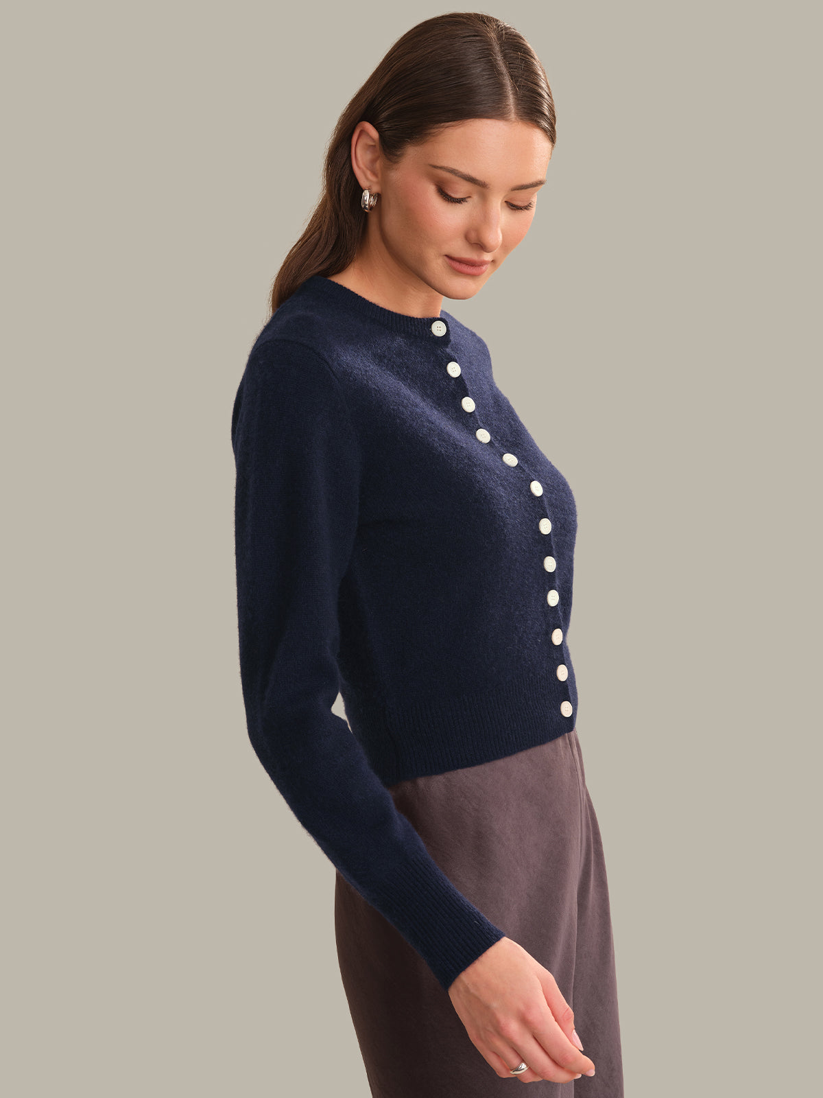A woman wearing a navy blue knit cardigan with white buttons down the front, paired with a dark gray skirt, photographed against a solid light gray background.
