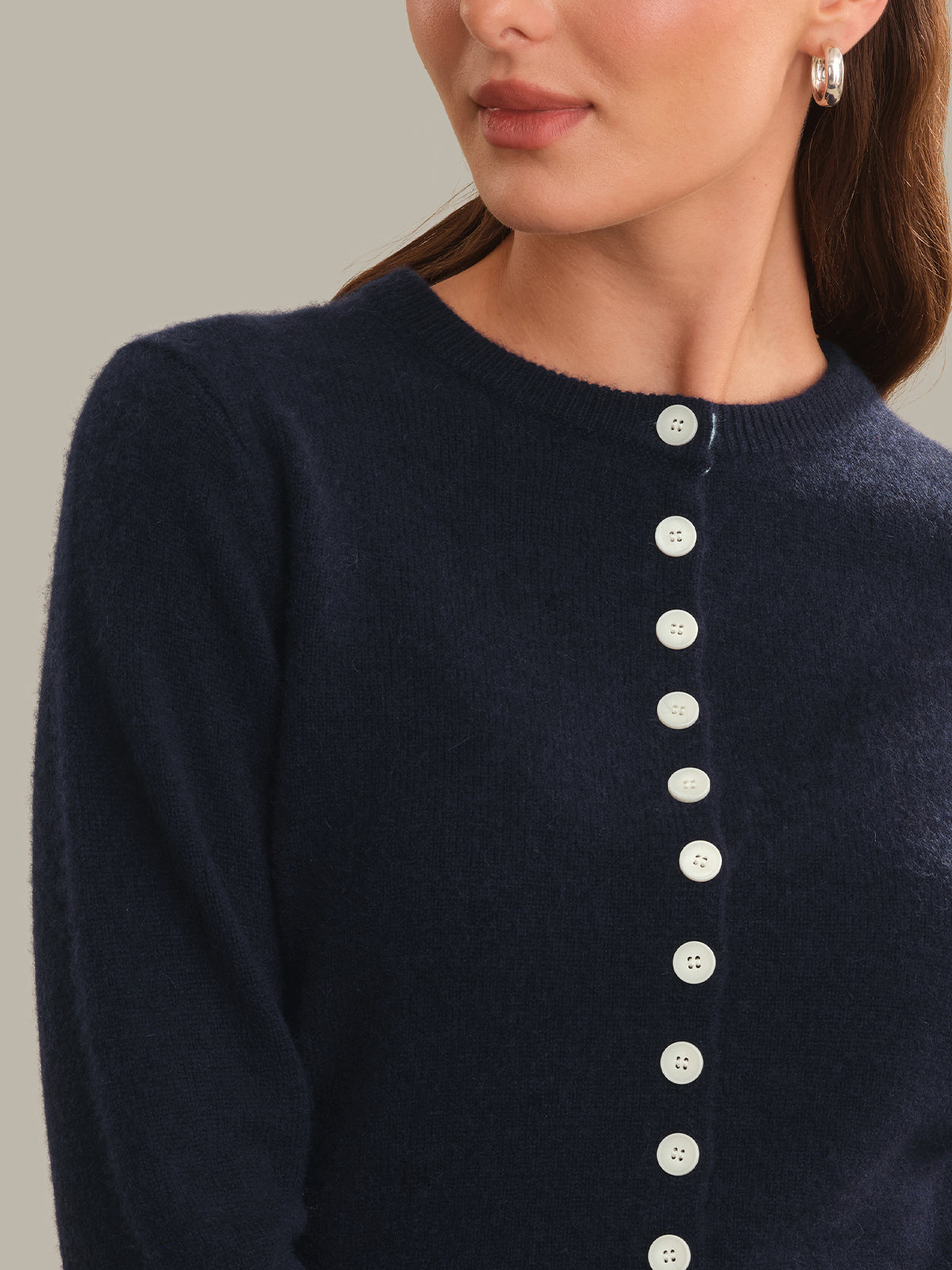 Close-up of a woman wearing a dark navy knit sweater with a vertical row of white buttons down the front, against a plain light gray background.