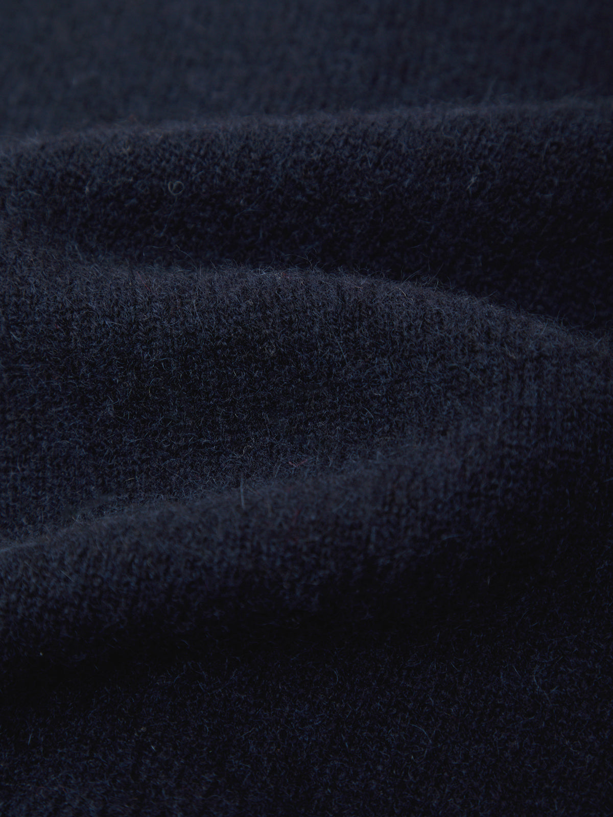 A close-up of dark navy blue knit fabric with soft folds and a fine textured weave.