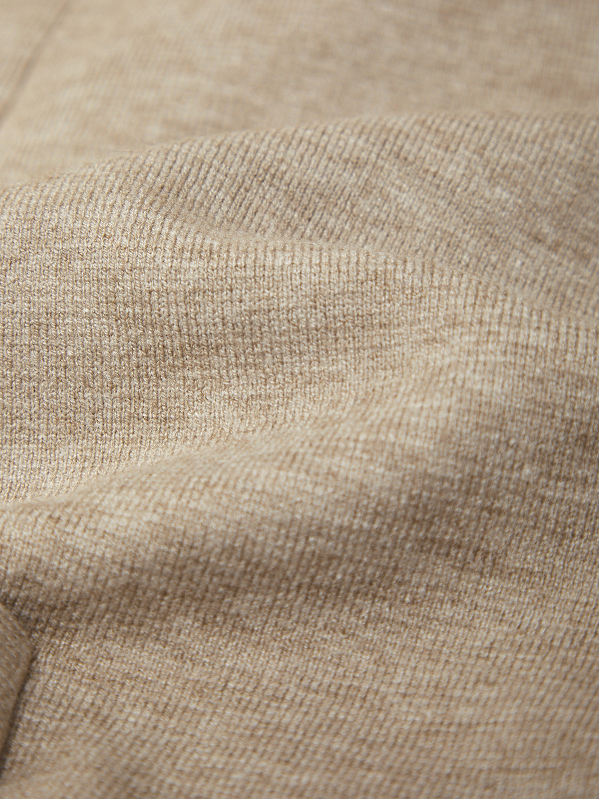 Close-up of a beige knit fabric texture with soft folds and ribbed stitching.