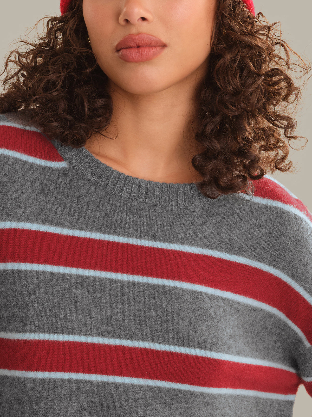 Close-up of a person wearing a gray knit sweater with bold red and thin white horizontal stripes.