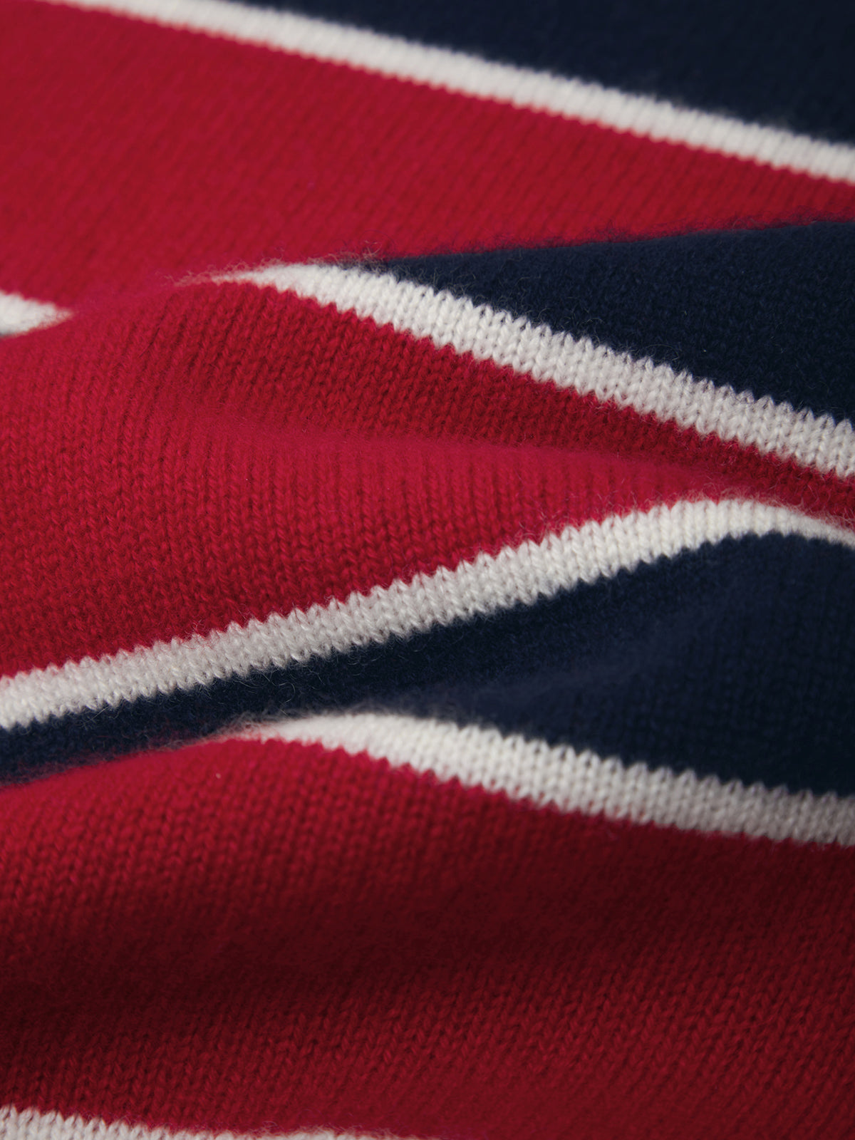 Close-up of a knitted fabric with diagonal stripes in red, navy blue, and white.