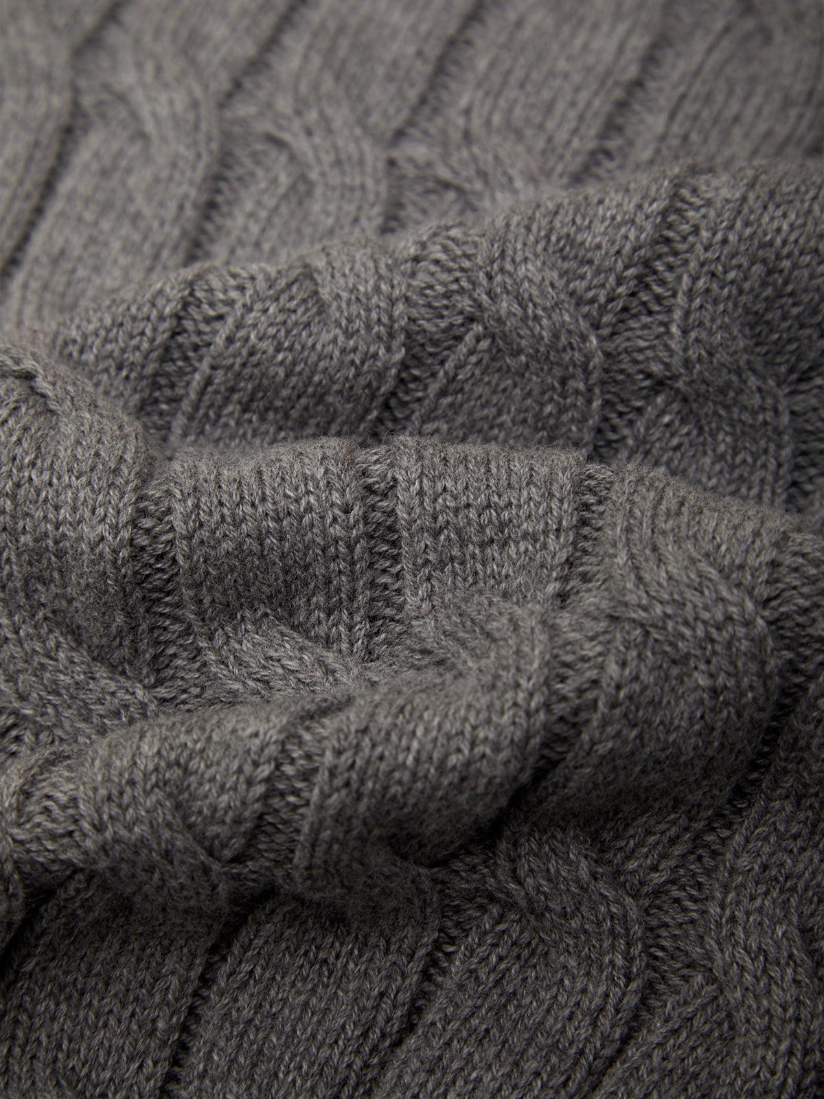 Close-up of a dark gray cable-knit fabric texture with detailed ribbed and twisted knit patterns.