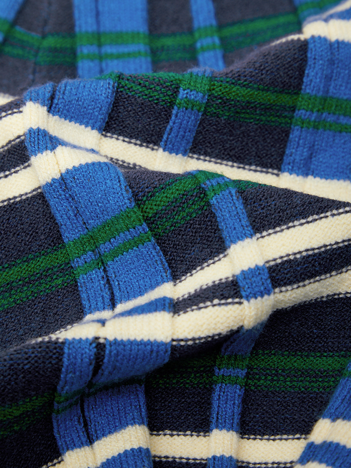 A close-up of a plaid knit fabric with blue, navy, green, and white stripes.