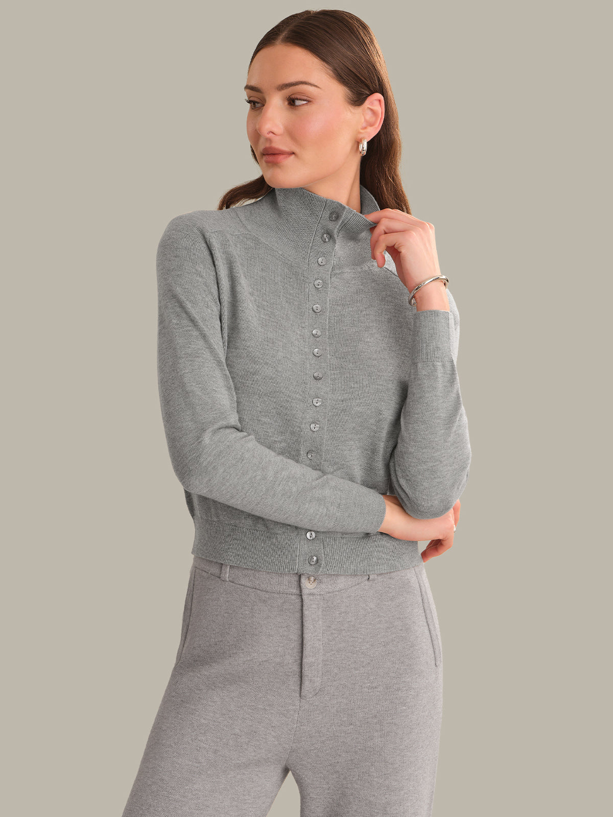 A woman modeling a light gray ribbed mock-neck button-front cardigan sweater with matching gray sweatpants, set against a solid light gray studio background.