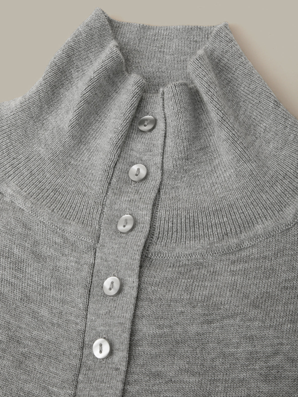 Close-up of a gray ribbed knit cardigan sweater featuring a high mock neck and a vertical row of white buttons down the front.