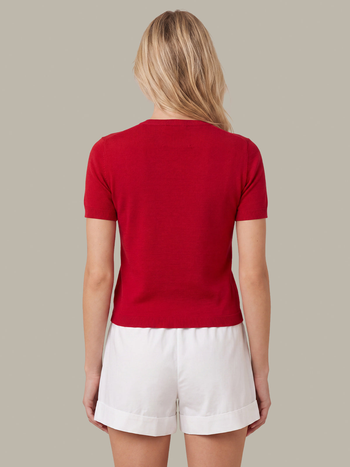 A woman shown from the back wearing a bright red short-sleeve crewneck top and white shorts against a solid light gray background.