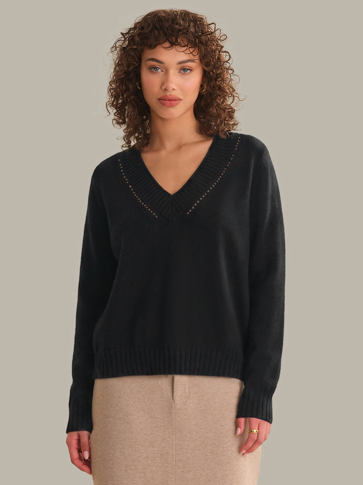 Woman wearing a black sweater with decorative trim on a beige background