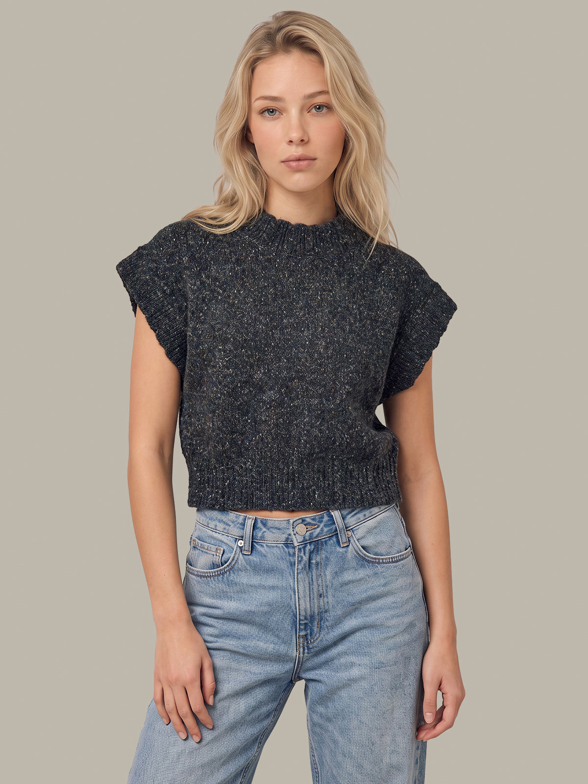 A blonde woman wearing a dark charcoal gray textured knit short-sleeve crop top and light wash blue jeans, standing against a solid light gray background.
