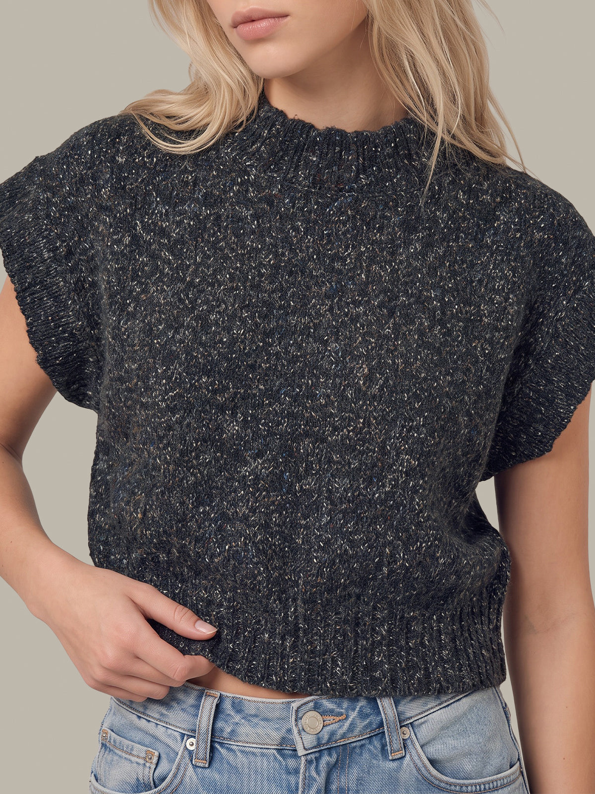 A close-up of a woman wearing a dark charcoal gray short-sleeve knit sweater with a textured heathered pattern, paired with light blue jeans.