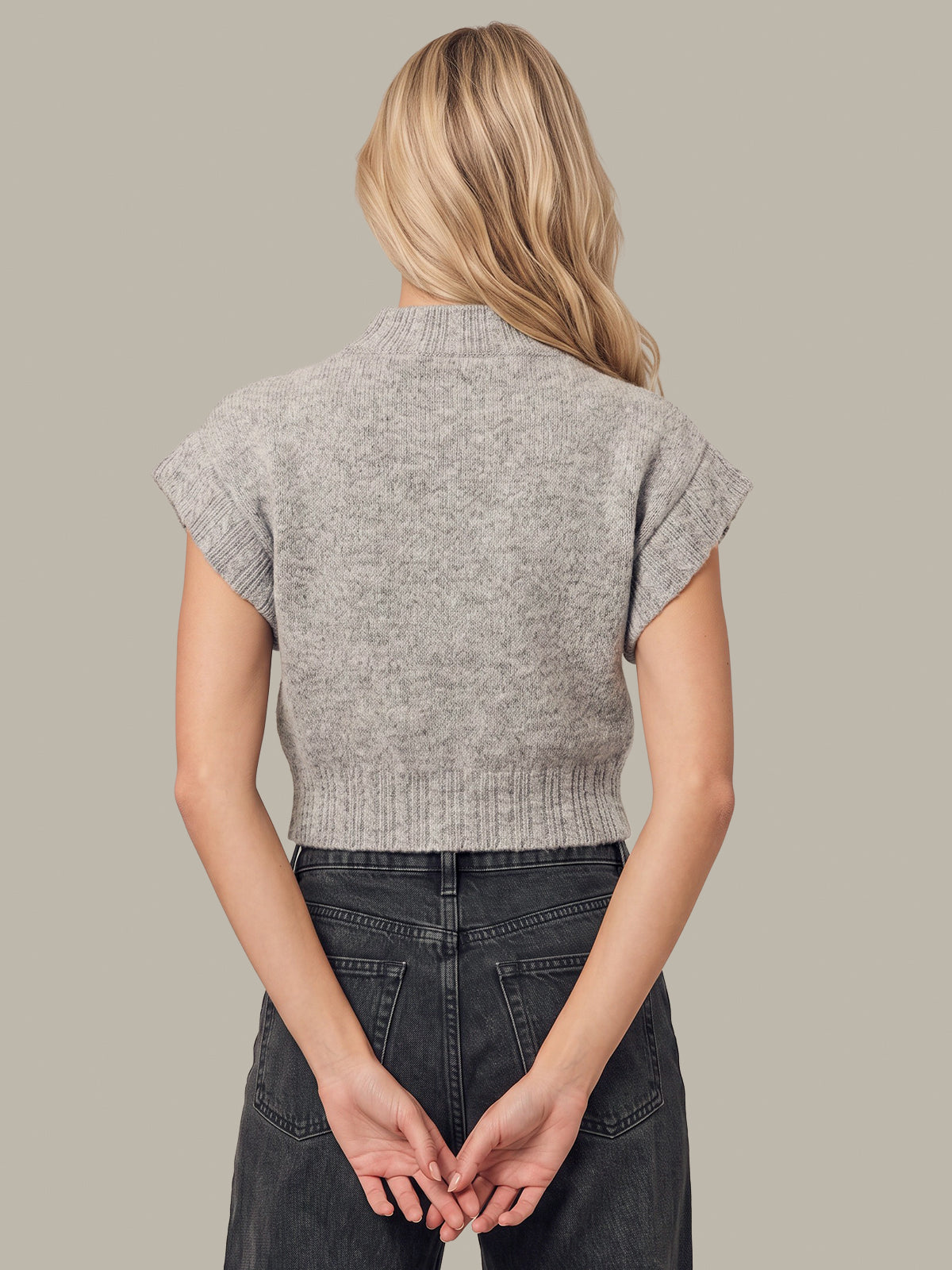 A woman shown from the back wearing a light gray ribbed knit cropped sweater with cap sleeves and dark gray jeans, set against a solid light gray background.