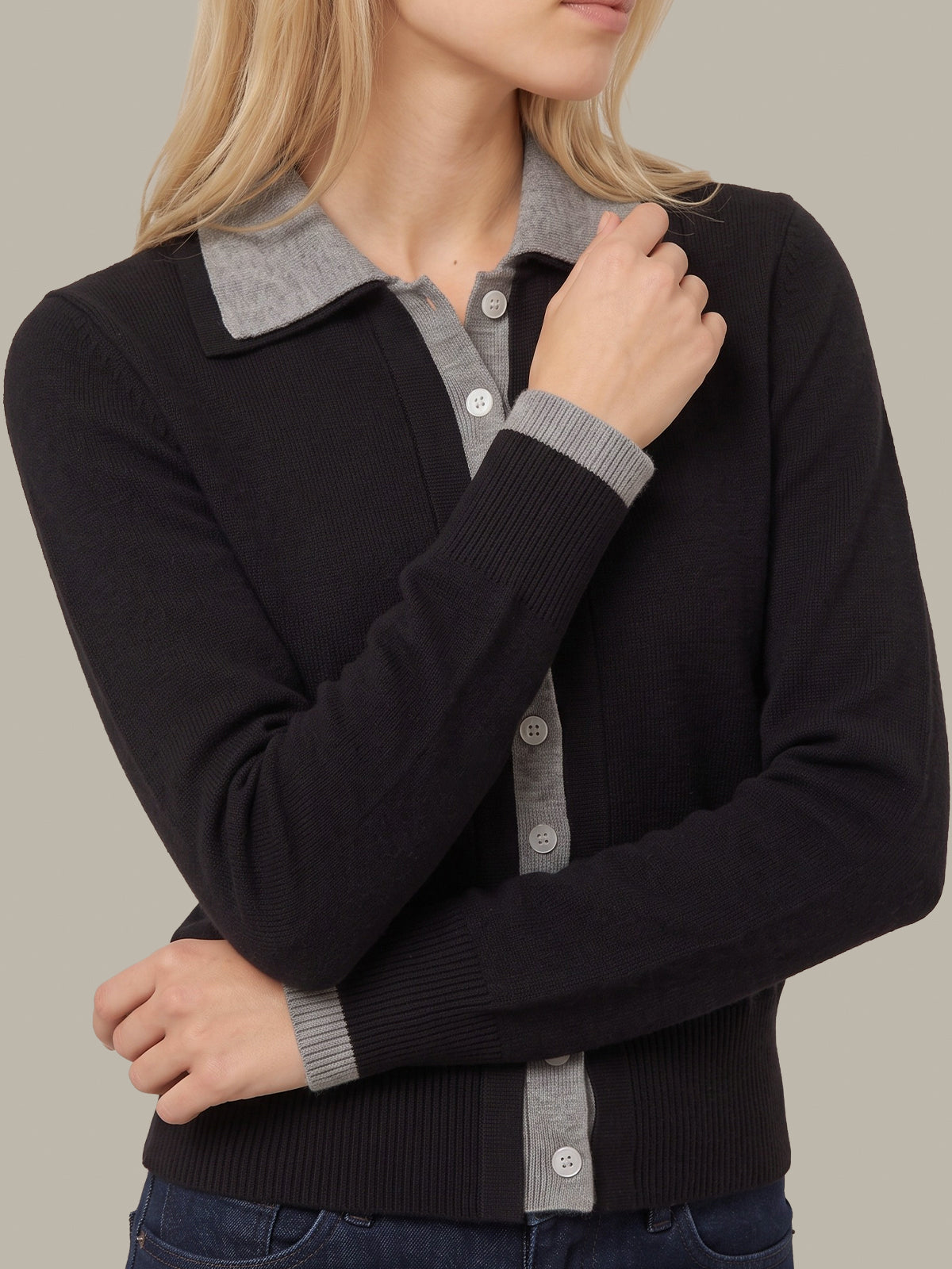 A woman wearing a black knit cardigan with a contrasting gray ribbed collar, button placket, and ribbed cuffs, shown against a plain beige background.