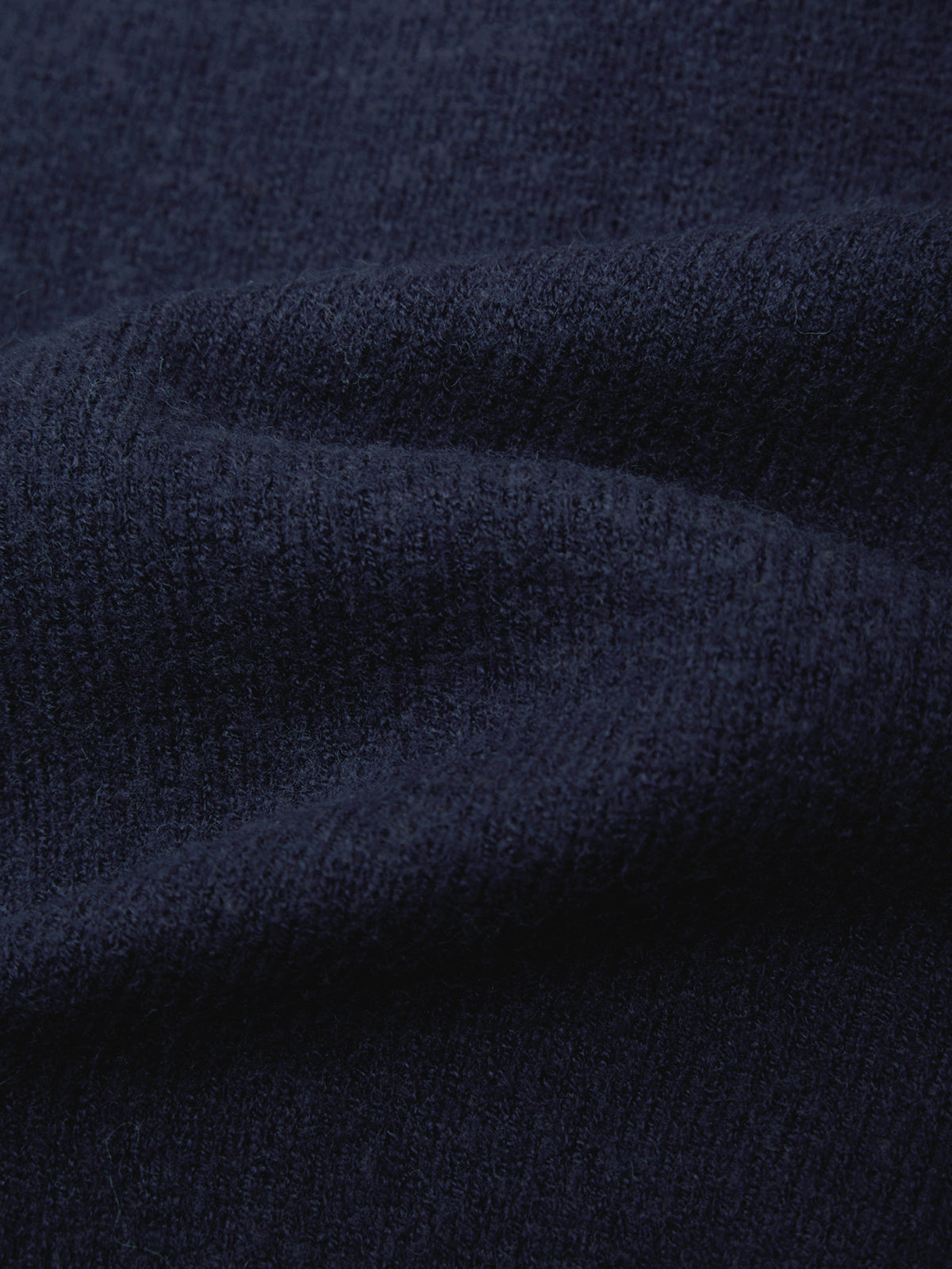 A close-up of dark navy blue knit fabric with soft folds and a ribbed texture.