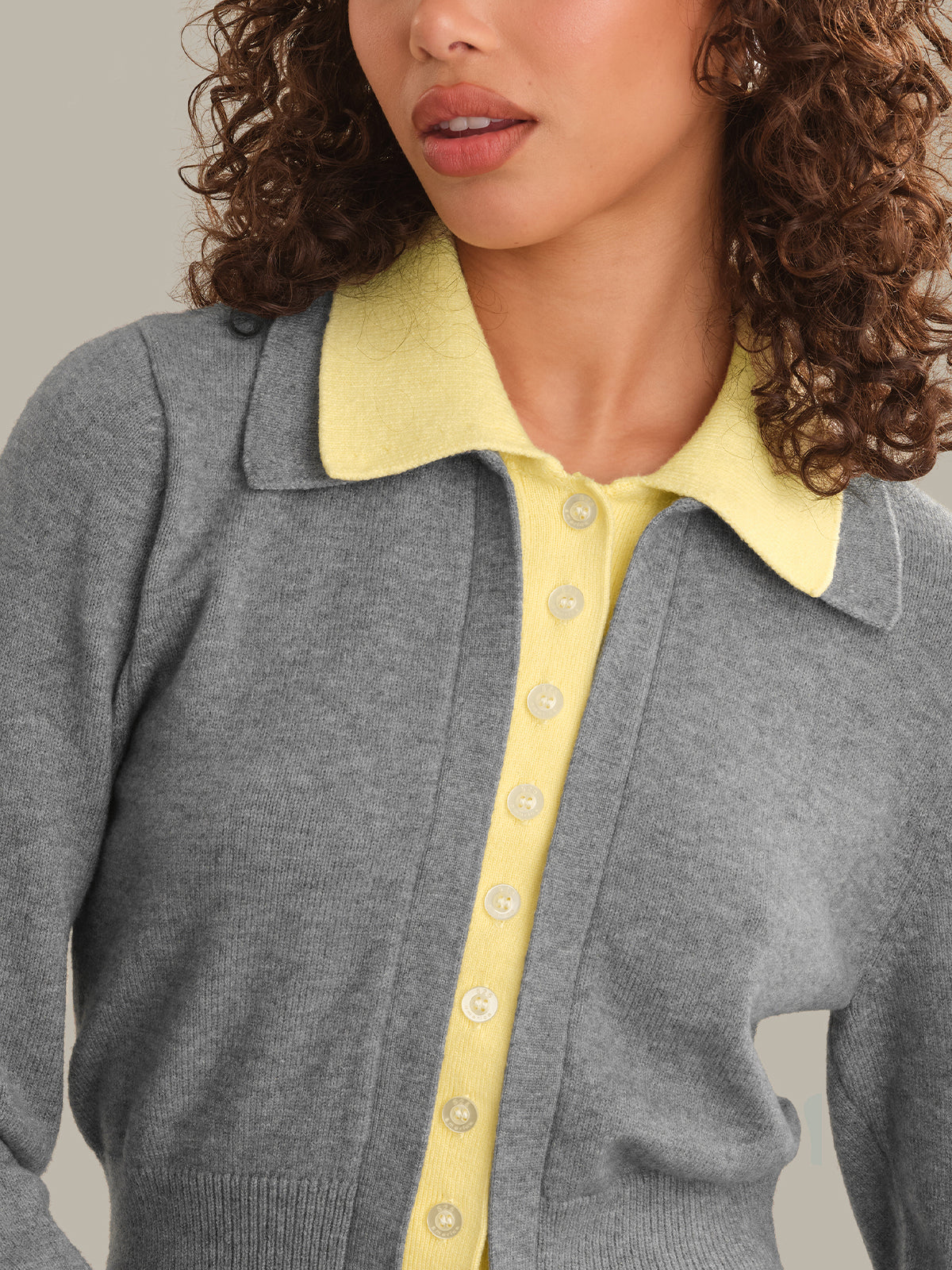 Close-up of a person wearing a gray knit cardigan with a pale yellow collar and matching pale yellow button placket over a pale yellow top.