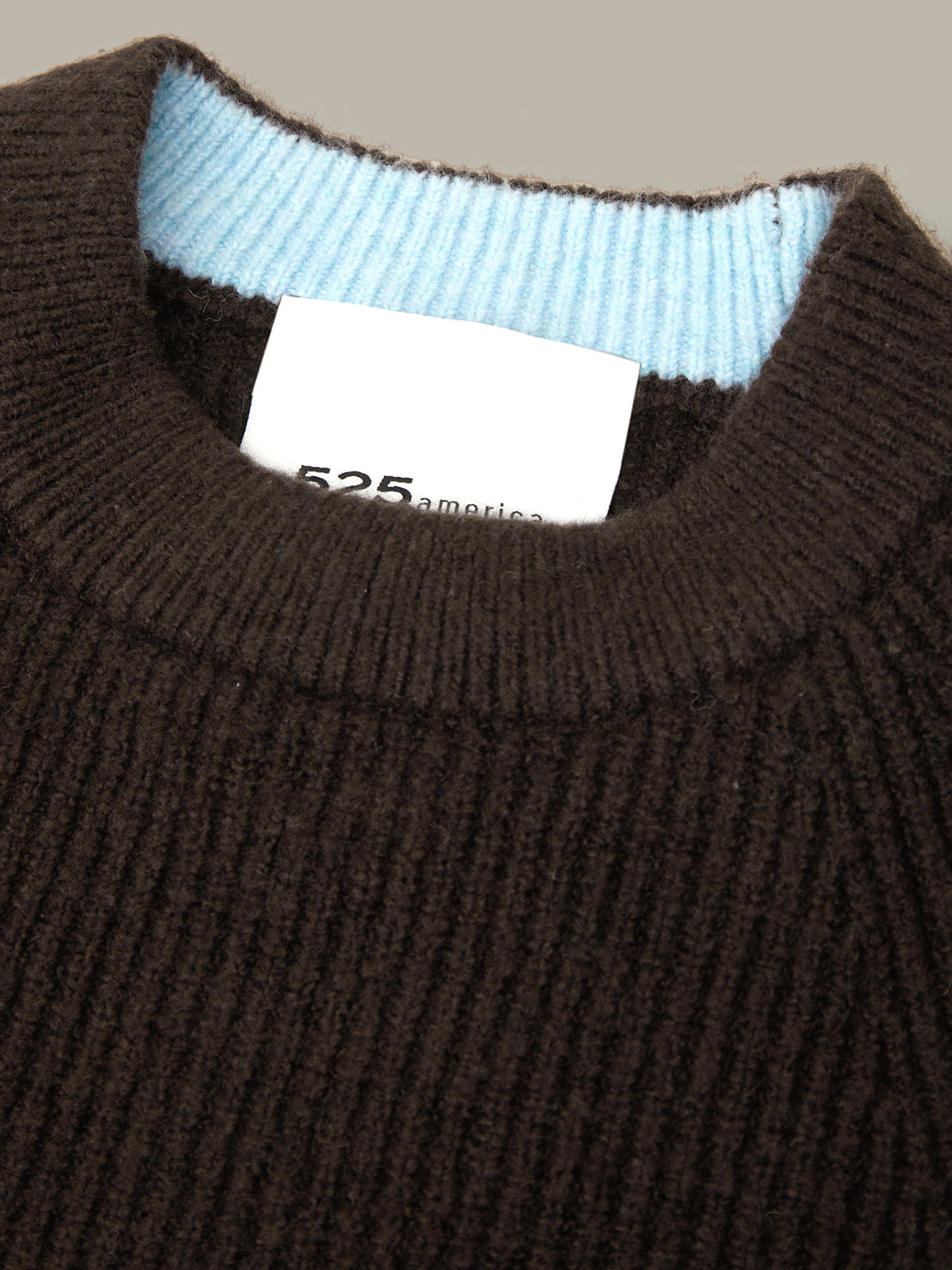 Close-up of a dark brown ribbed knit sweater with a light blue inner collar lining and a white neck label reading '525 america'.