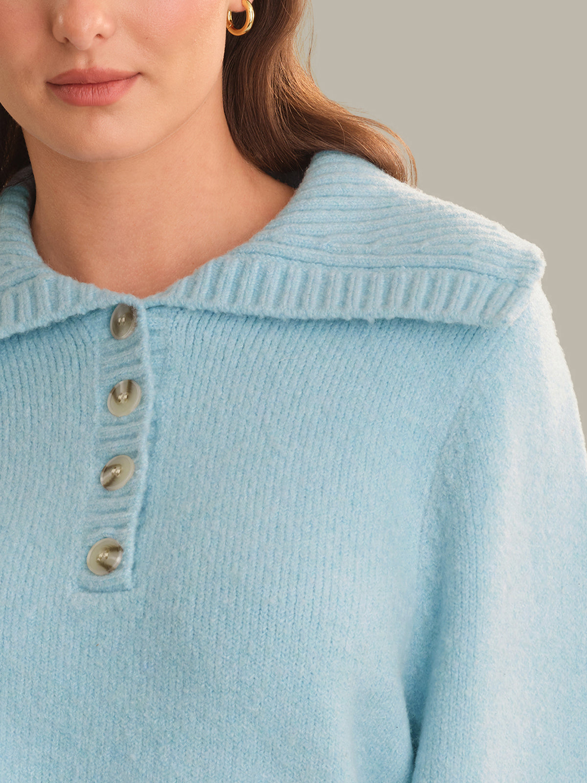 Close-up of a woman wearing a light blue knit sweater with a wide ribbed collar and a three-button placket.