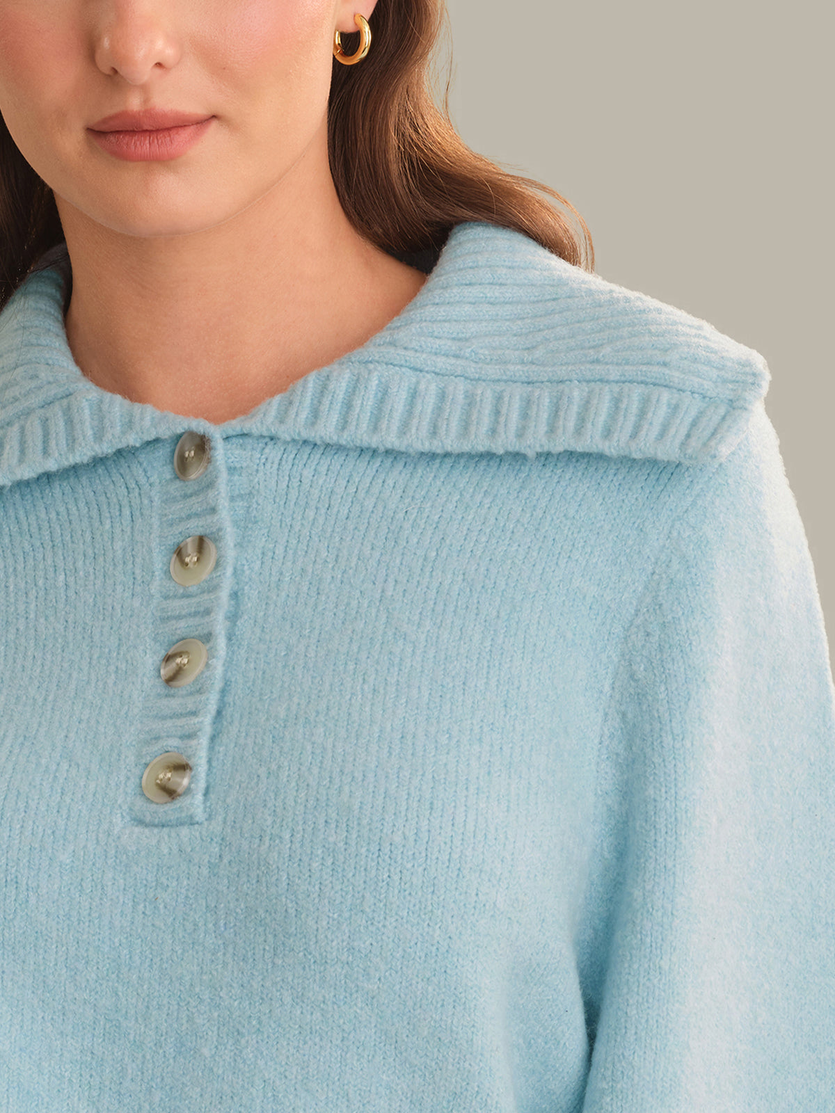 Close-up of a woman wearing a light blue ribbed knit sweater with a collar and three front buttons.