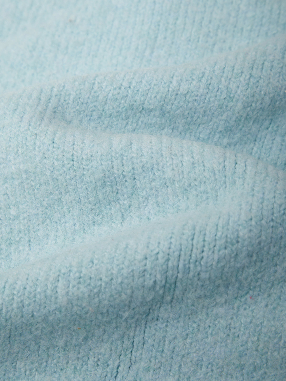 A close-up of light blue knit fabric with soft folds and a fine ribbed texture.
