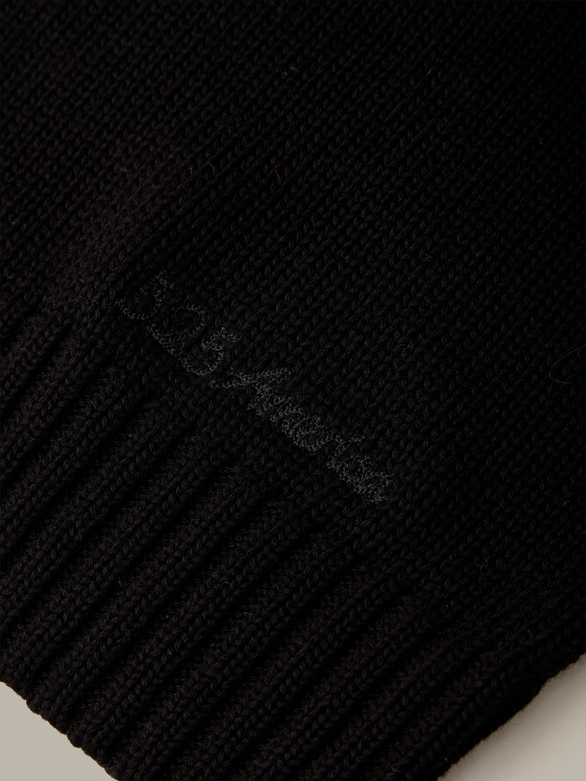 Close-up of a black ribbed knit beanie with subtle tonal embroidery reading '5.15 America' on the side.
