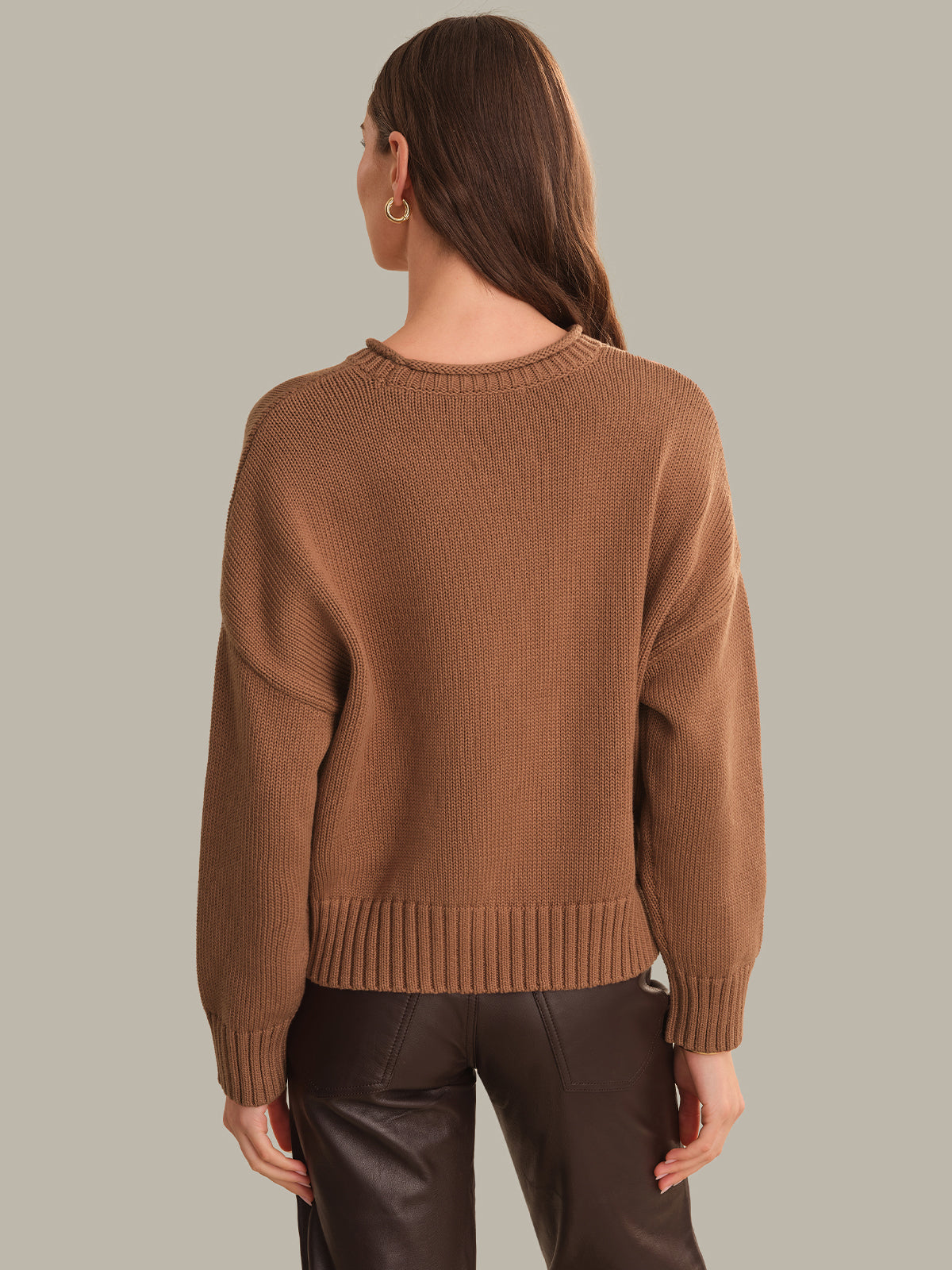 A woman shown from the back wearing a brown ribbed knit sweater and dark brown pants against a solid light gray background.