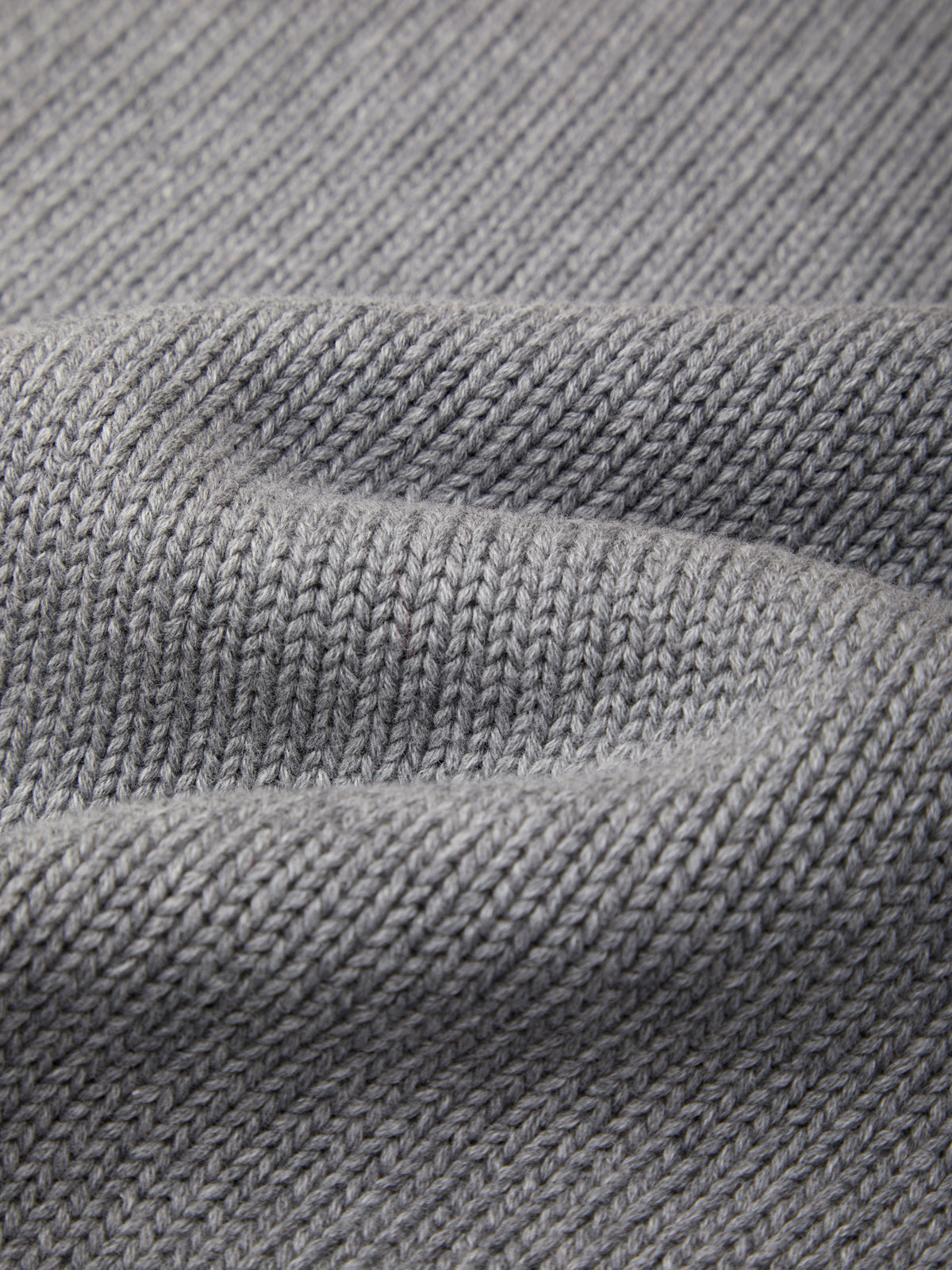 Close-up of a gray knit fabric texture with soft folds showing the woven pattern.